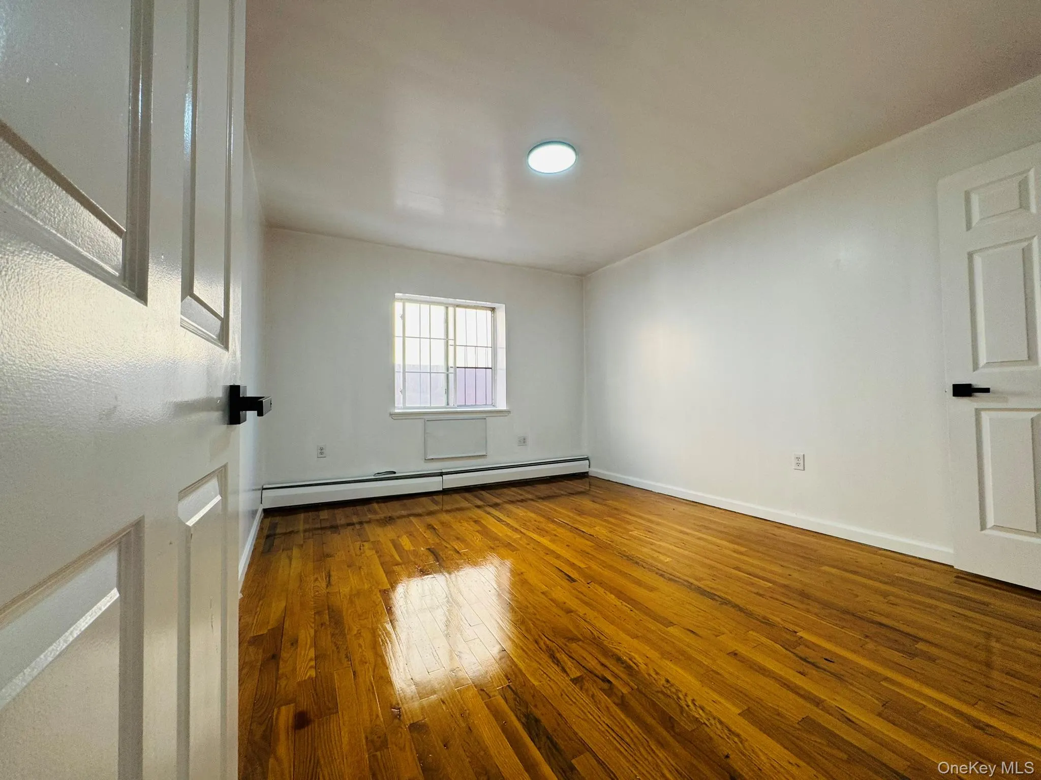 Empty room with hardwood / wood-style floors and a baseboard radiator Empty room with hardwood / wood-style floors and a baseboard radiator
