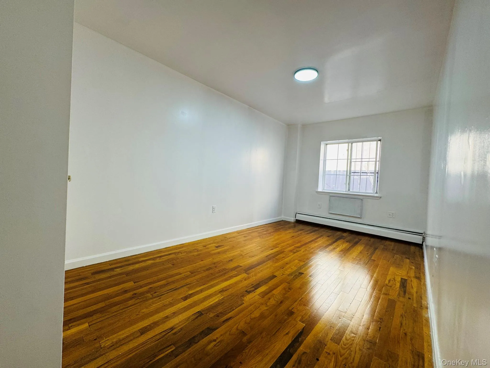 Empty room featuring dark wood-style flooring and a baseboard radiator Empty room featuring dark wood-style flooring and a baseboard radiator