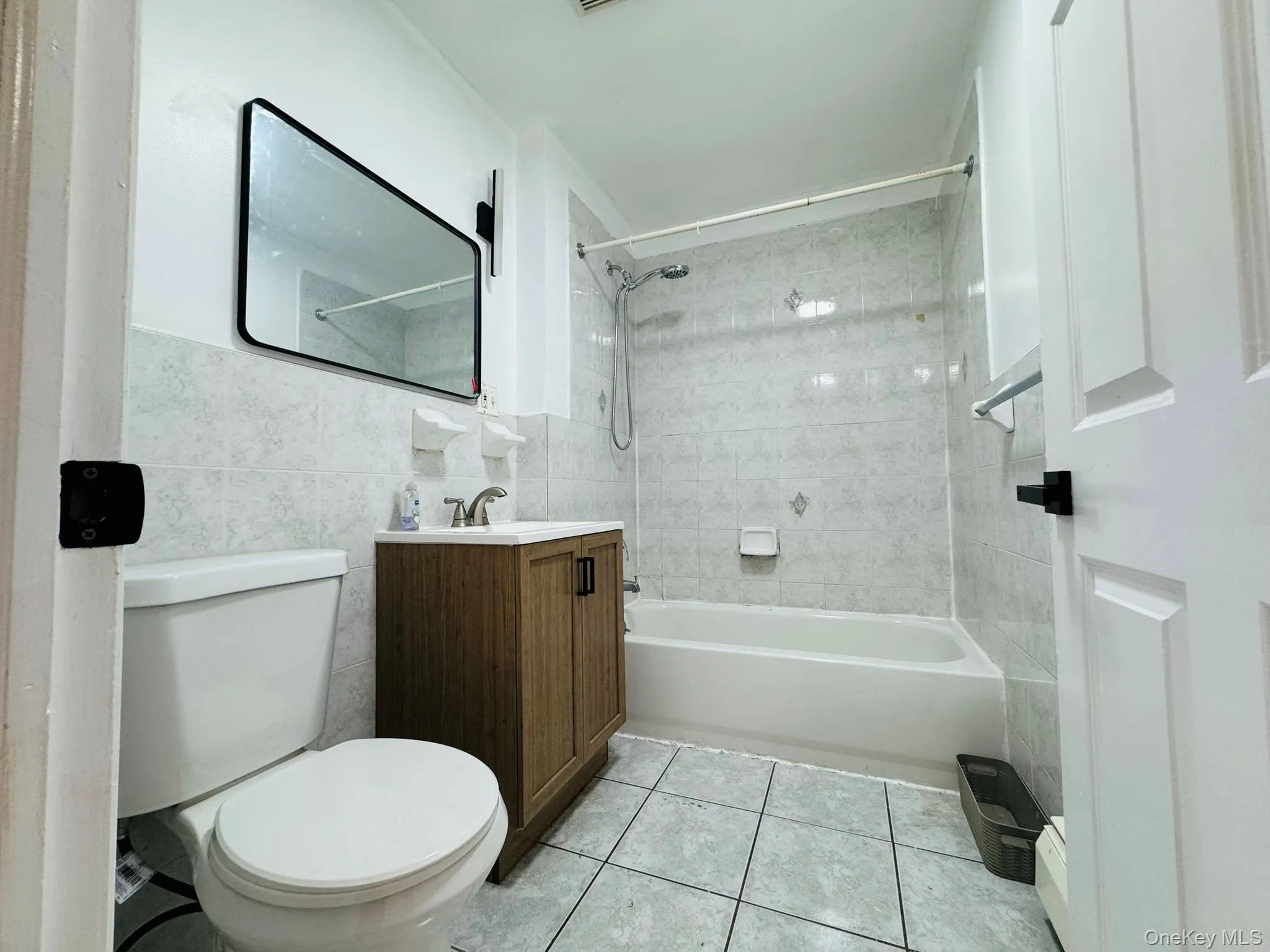 Full bath with vanity, washtub / shower combination, tile walls, and light tile patterned floors Full bath with vanity, washtub / shower combination, tile walls, and light tile patterned floors