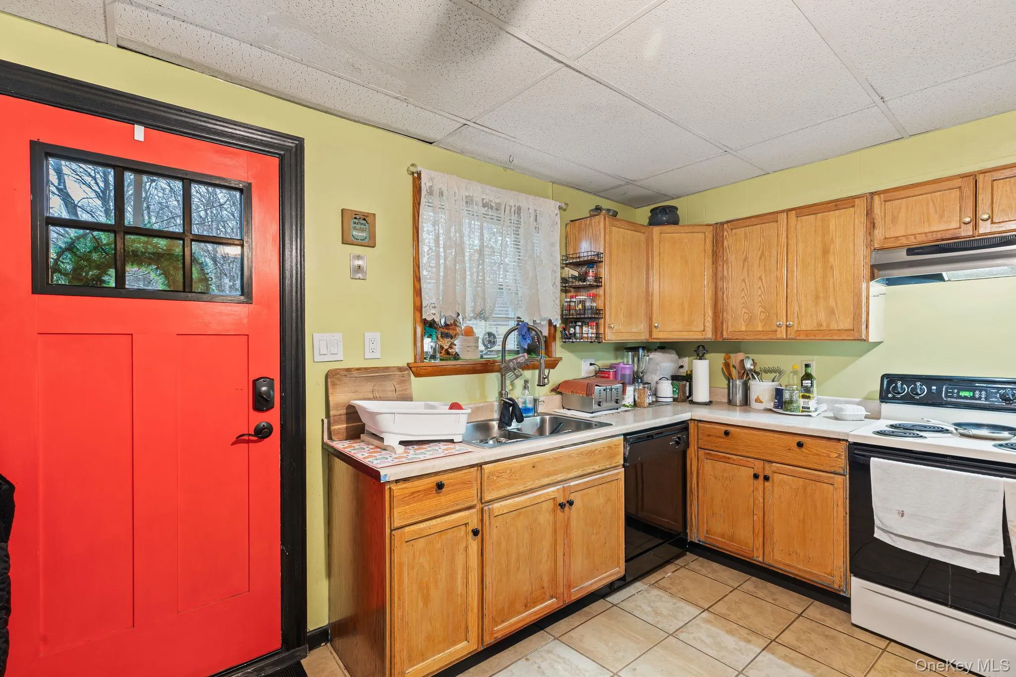 Kitchen with electric range, a paneled ceiling, black dishwasher, under cabinet range hood, and light tile patterned flooring Kitchen with electric range, a paneled ceiling, black dishwasher, under cabinet range hood, and light tile patterned flooring