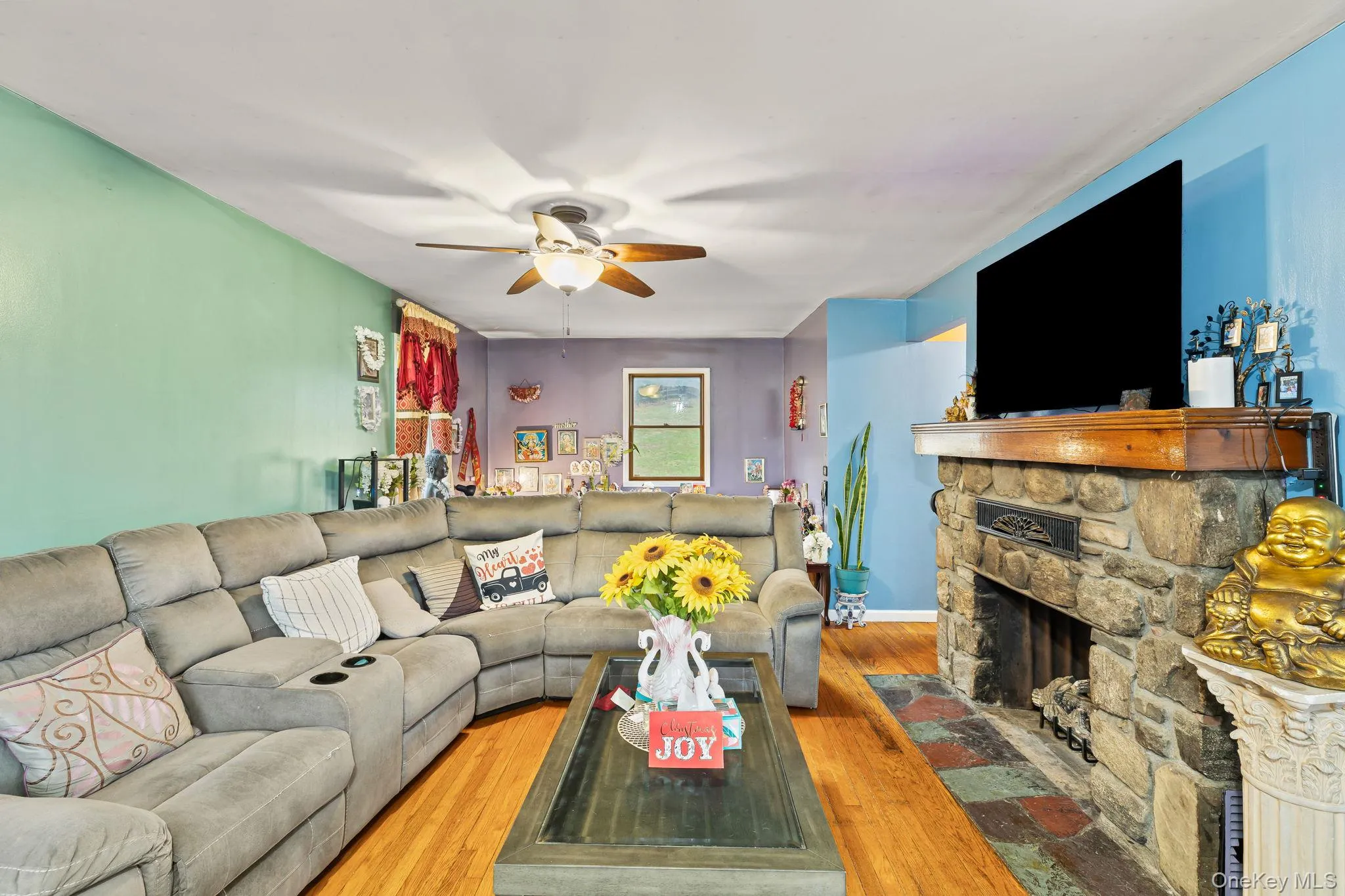 Living room with wood-type flooring, a ceiling fan, and a stone fireplace Living room with wood-type flooring, a ceiling fan, and a stone fireplace