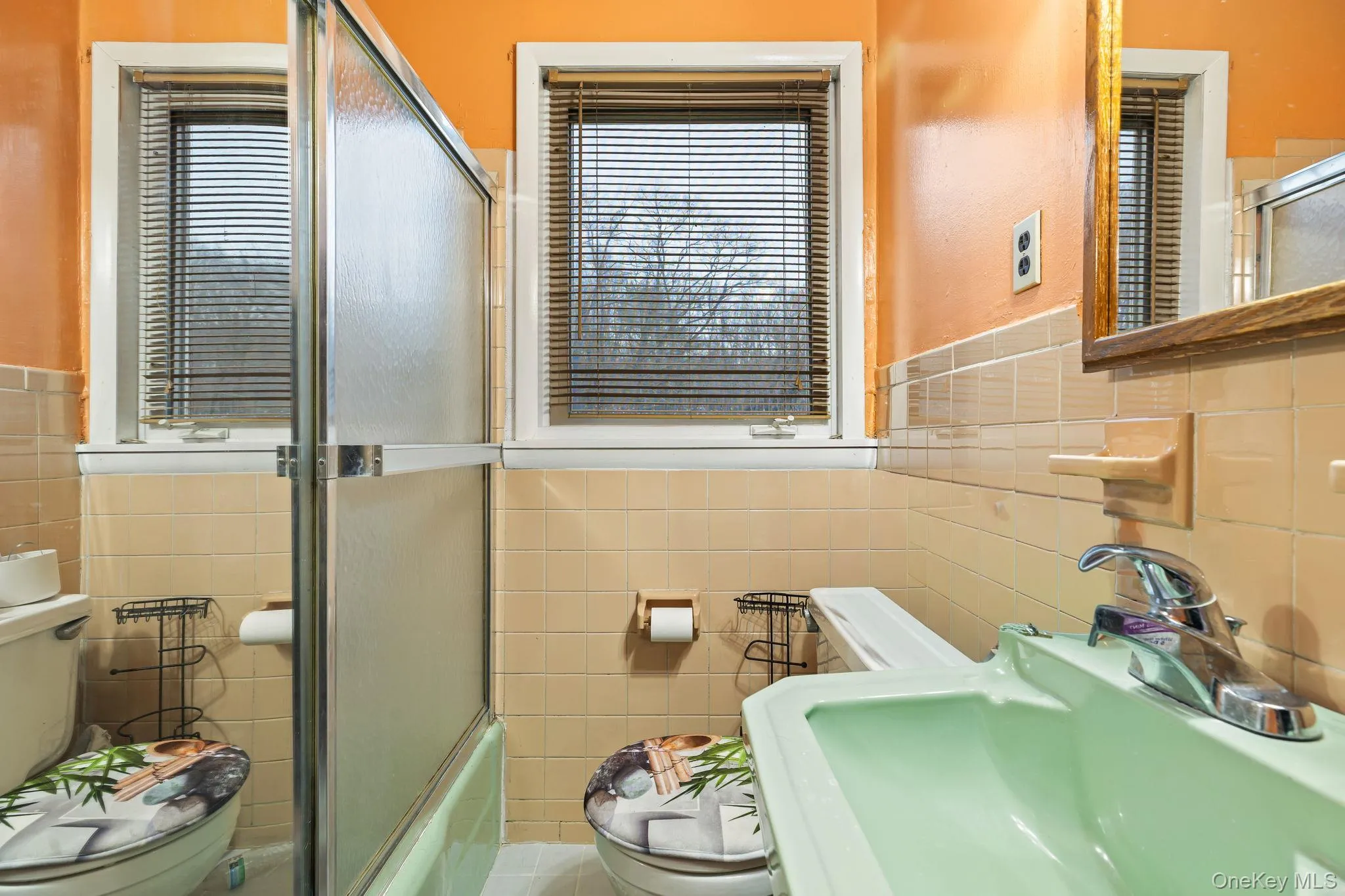 Bathroom featuring tile walls, enclosed tub / shower combo, and wainscoting Bathroom featuring tile walls, enclosed tub / shower combo, and wainscoting