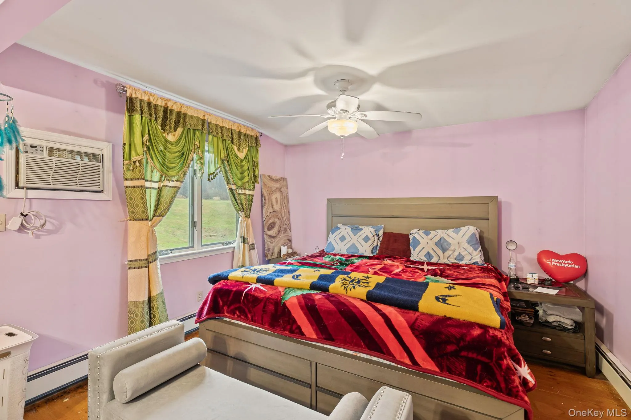 Bedroom with baseboard heating, an AC wall unit, a ceiling fan, and wood finished floors Bedroom with baseboard heating, an AC wall unit, a ceiling fan, and wood finished floors