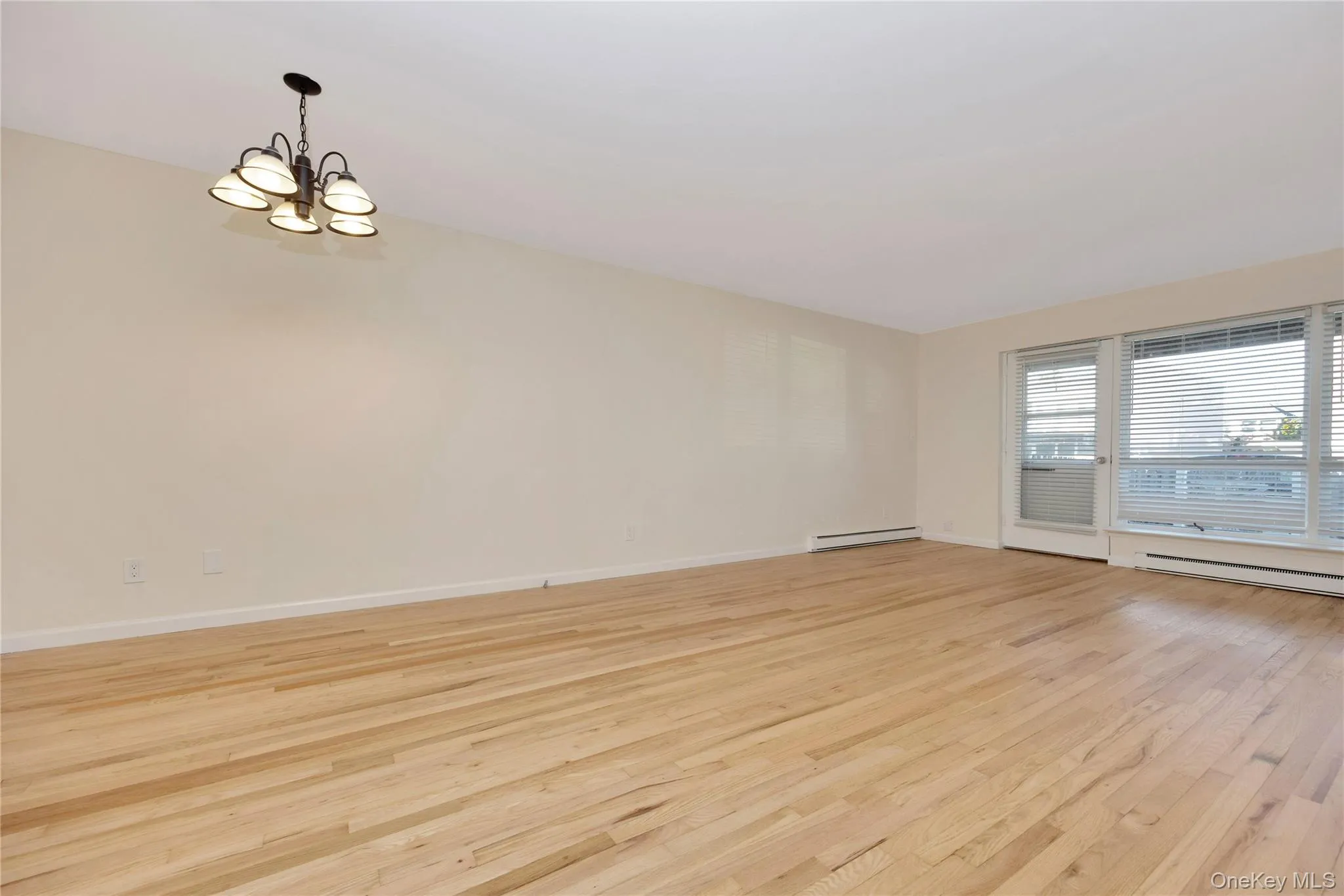 Spare room with light wood finished floors, a chandelier, and a baseboard radiator Spare room with light wood finished floors, a chandelier, and a baseboard radiator