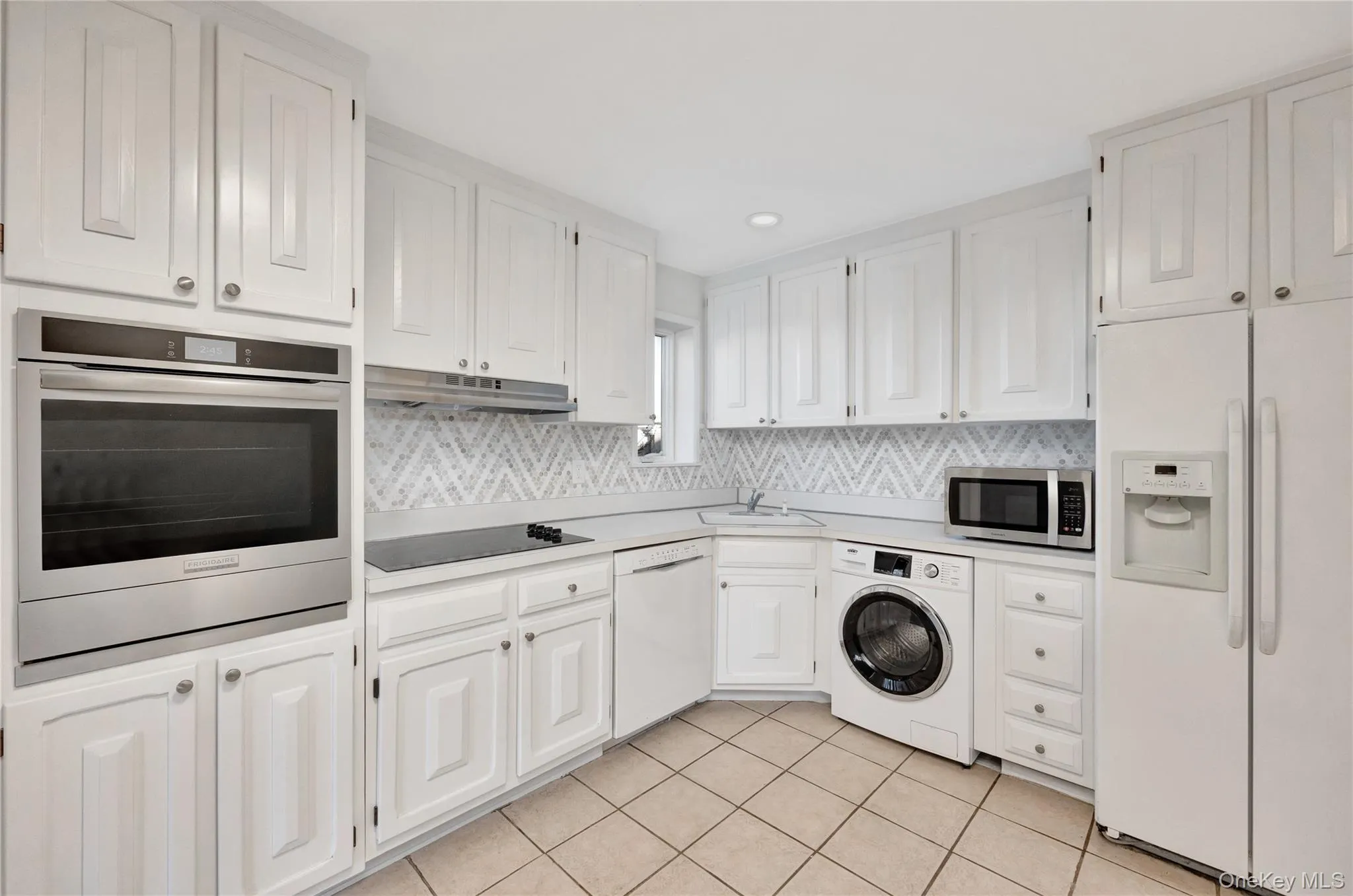 Kitchen with appliances with stainless steel finishes, washer / clothes dryer, white cabinetry, and under cabinet range hood Kitchen with appliances with stainless steel finishes, washer / clothes dryer, white cabinetry, and under cabinet range hood