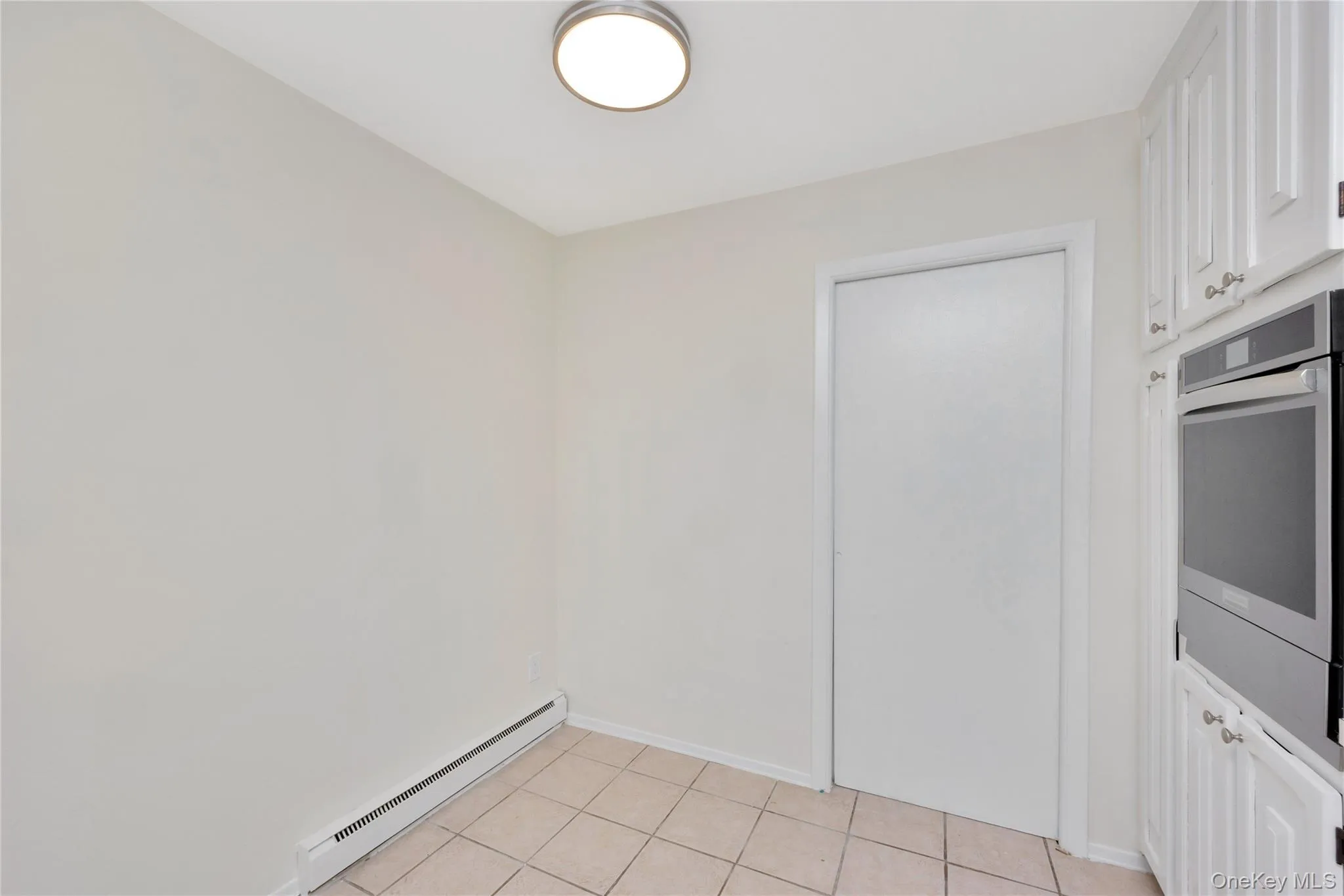 Kitchen featuring baseboard heating, white cabinetry, oven, and light tile patterned flooring Kitchen featuring baseboard heating, white cabinetry, oven, and light tile patterned flooring