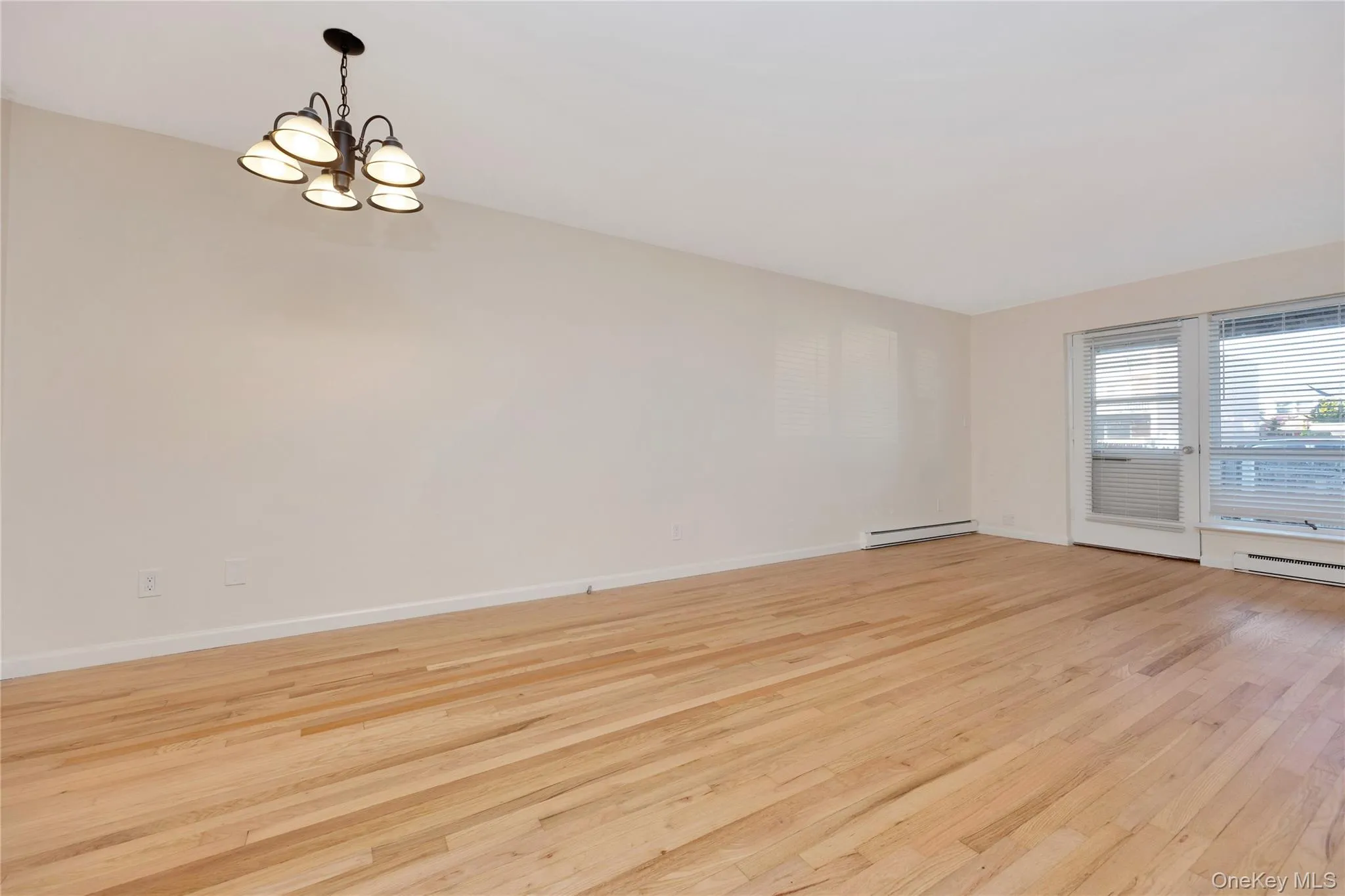 Unfurnished room with light wood-type flooring, a chandelier, and a baseboard heating unit Unfurnished room with light wood-type flooring, a chandelier, and a baseboard heating unit