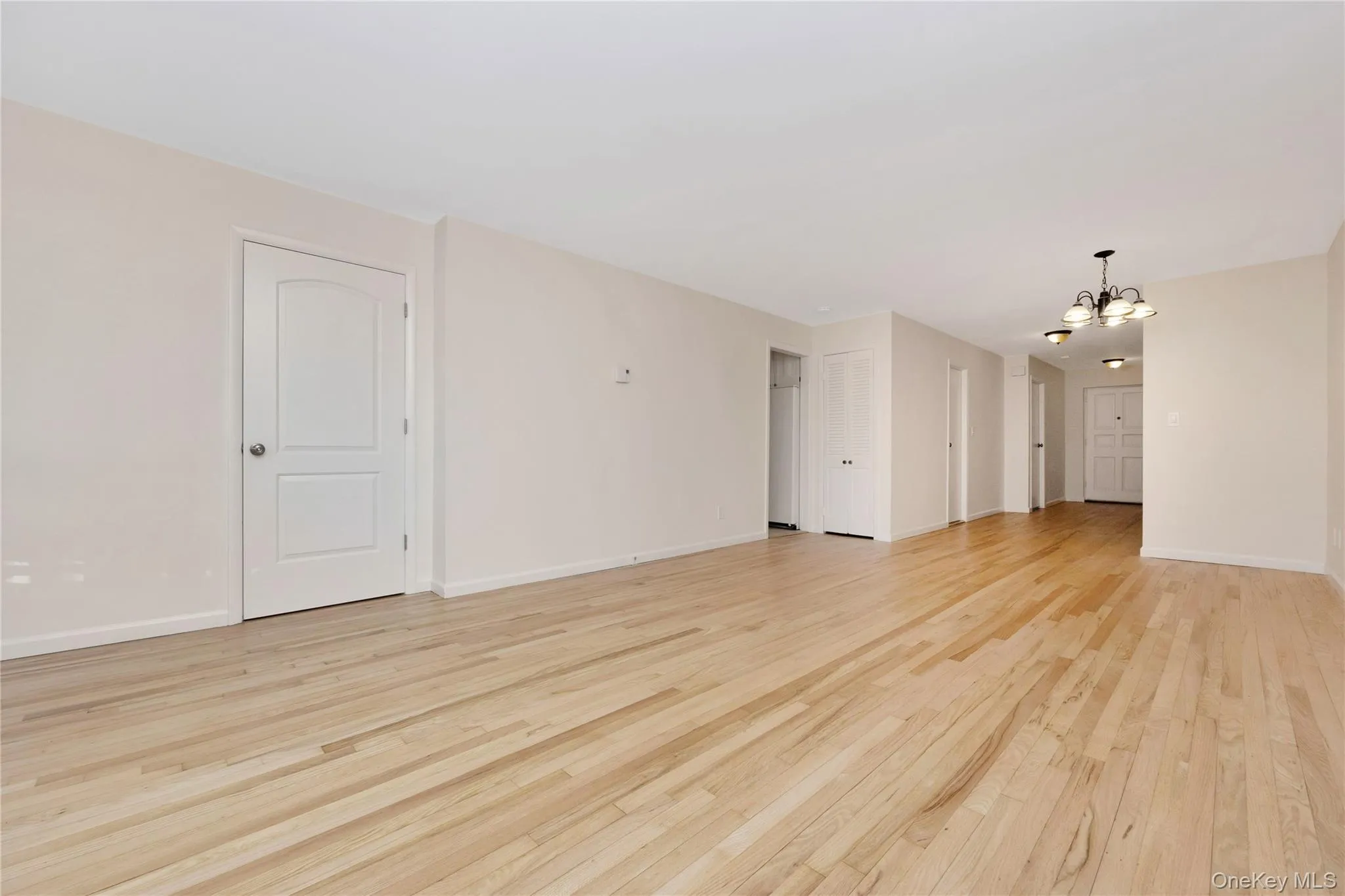 Unfurnished living room featuring a chandelier and light wood finished floors Unfurnished living room featuring a chandelier and light wood finished floors
