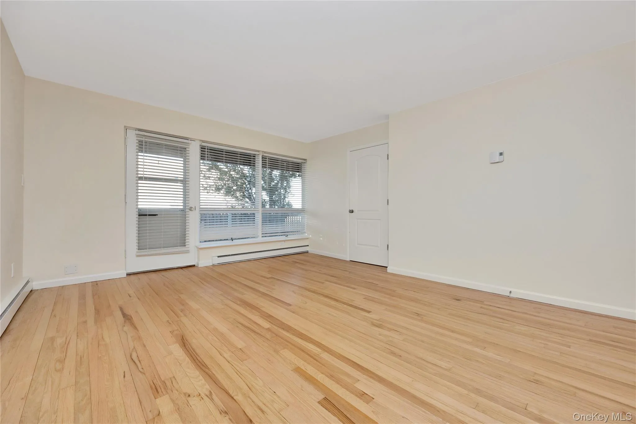 Unfurnished room with light wood finished floors and a baseboard heating unit Unfurnished room with light wood finished floors and a baseboard heating unit