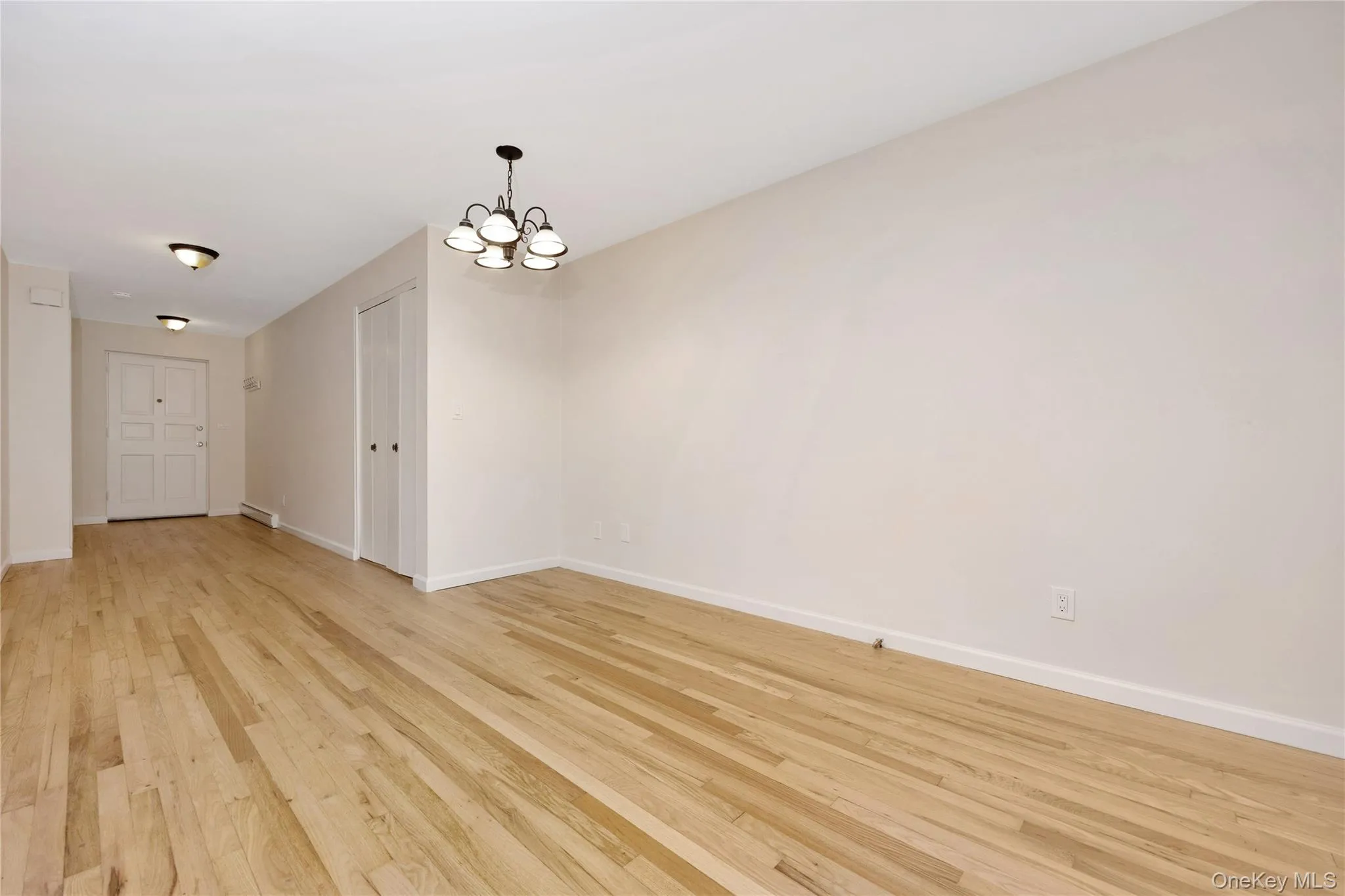 Spare room featuring a chandelier, light wood-type flooring, and a baseboard heating unit Spare room featuring a chandelier, light wood-type flooring, and a baseboard heating unit