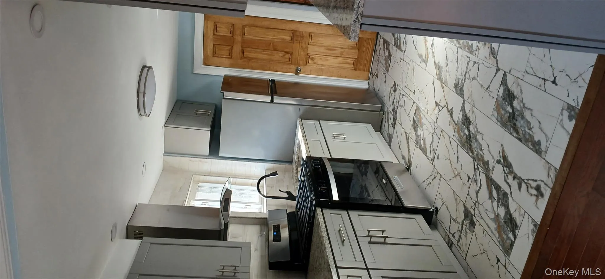 Kitchen featuring stainless steel appliances, ventilation hood, gray cabinets, light marble finish floors, and light stone countertops Kitchen featuring stainless steel appliances, ventilation hood, gray cabinets, light marble finish floors, and light stone countertops