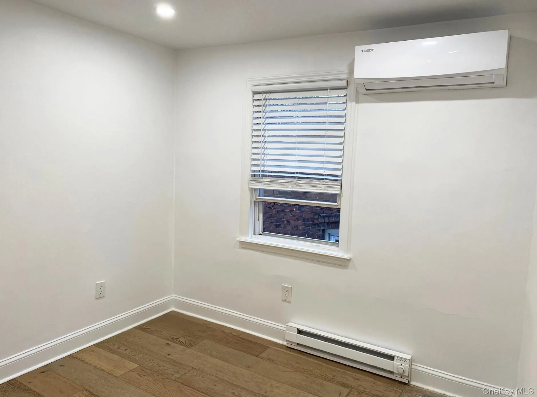 Unfurnished room with baseboard heating, wood-type flooring, and a wall mounted air conditioner Unfurnished room with baseboard heating, wood-type flooring, and a wall mounted air conditioner