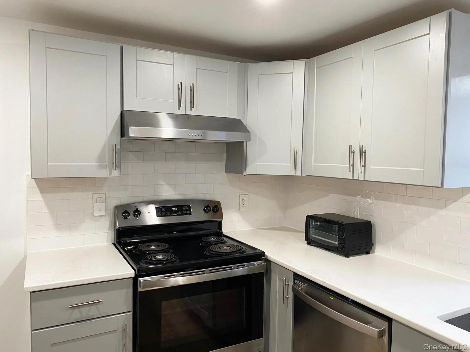 Kitchen featuring stainless steel appliances, under cabinet range hood, decorative backsplash, and gray cabinetry Kitchen featuring stainless steel appliances, under cabinet range hood, decorative backsplash, and gray cabinetry