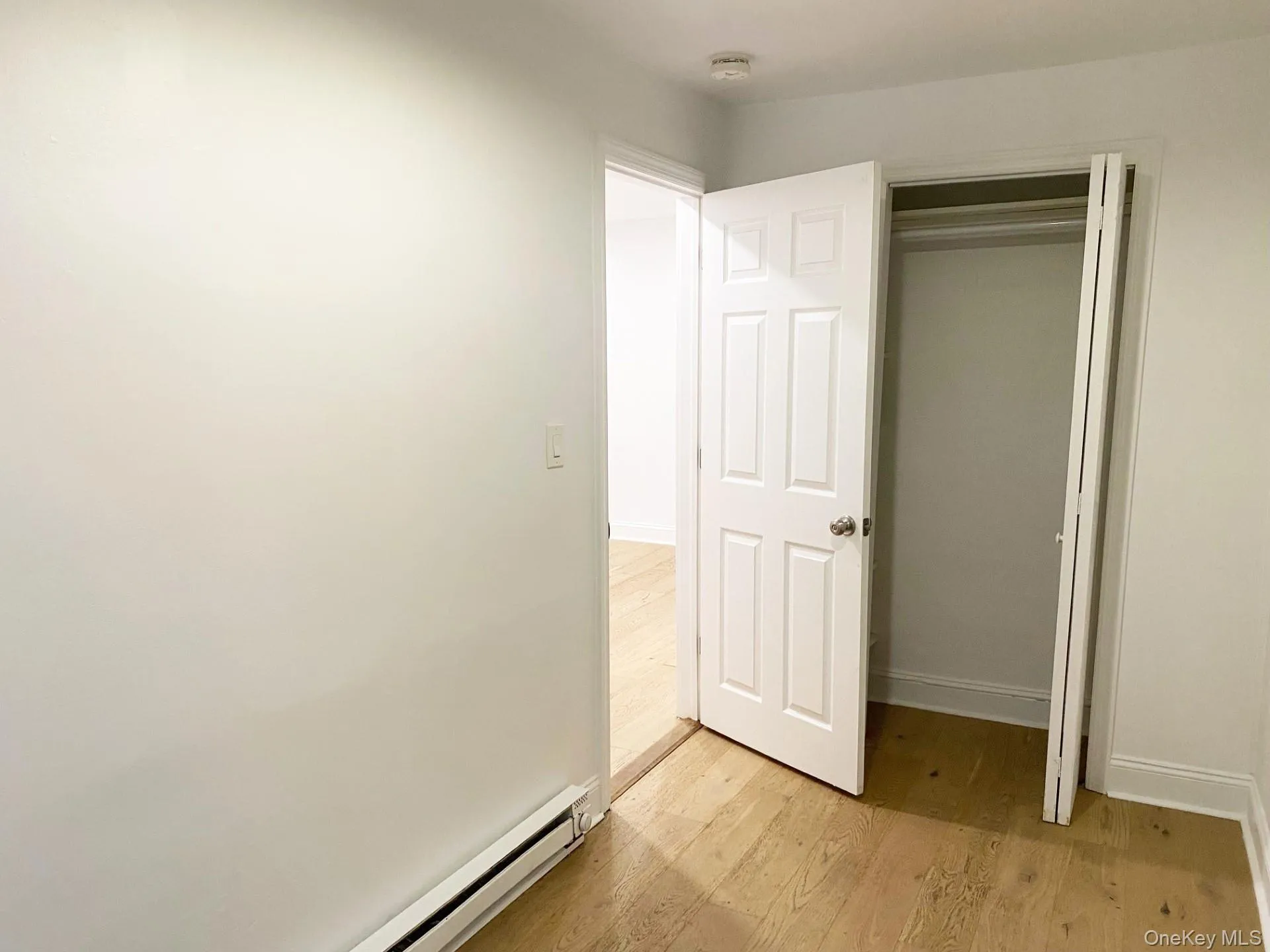 Unfurnished bedroom with baseboard heating, a closet, and light wood-type flooring Unfurnished bedroom with baseboard heating, a closet, and light wood-type flooring