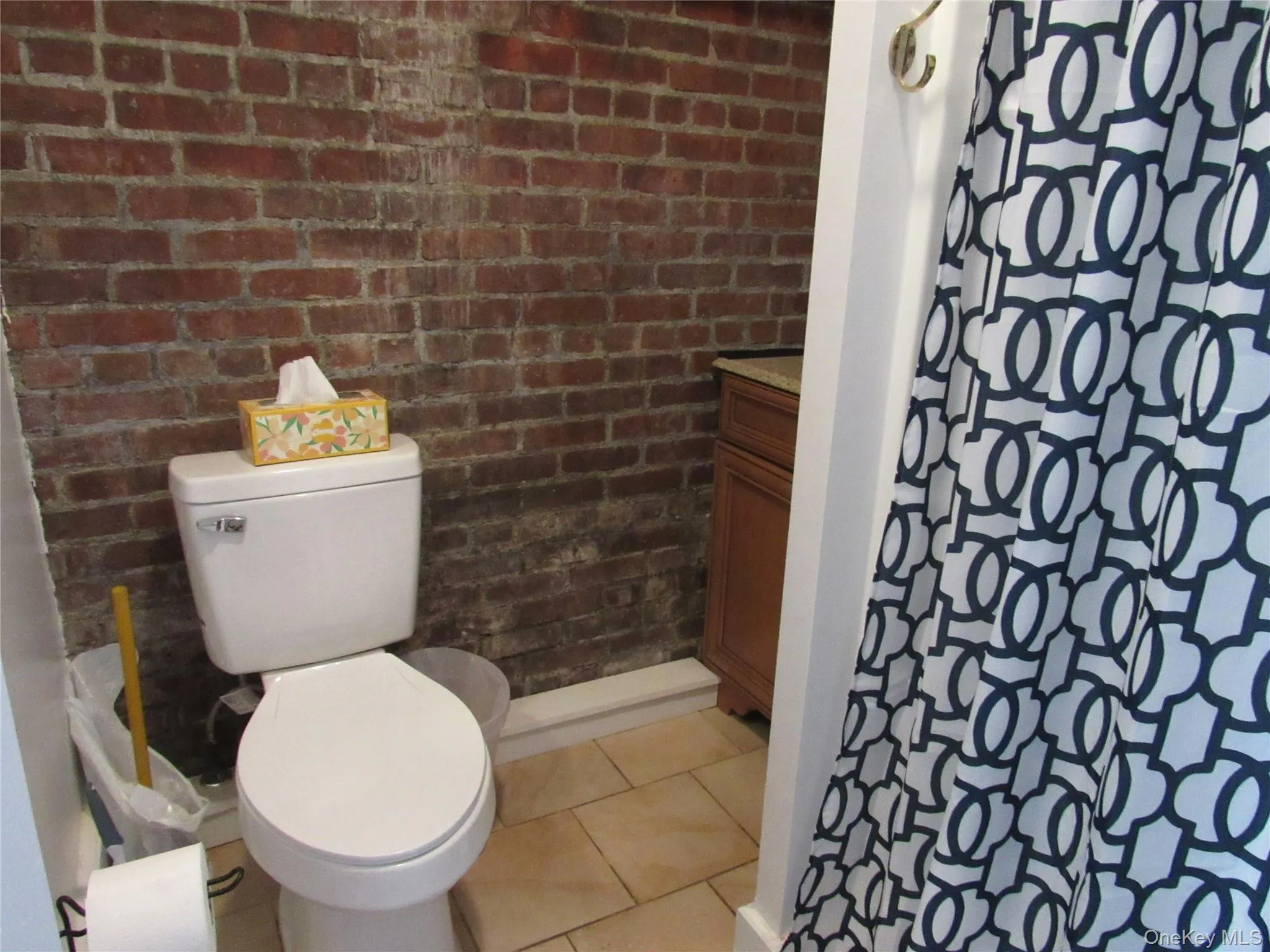 Bathroom with brick wall, curtained shower, light tile patterned flooring, and vanity Bathroom with brick wall, curtained shower, light tile patterned flooring, and vanity