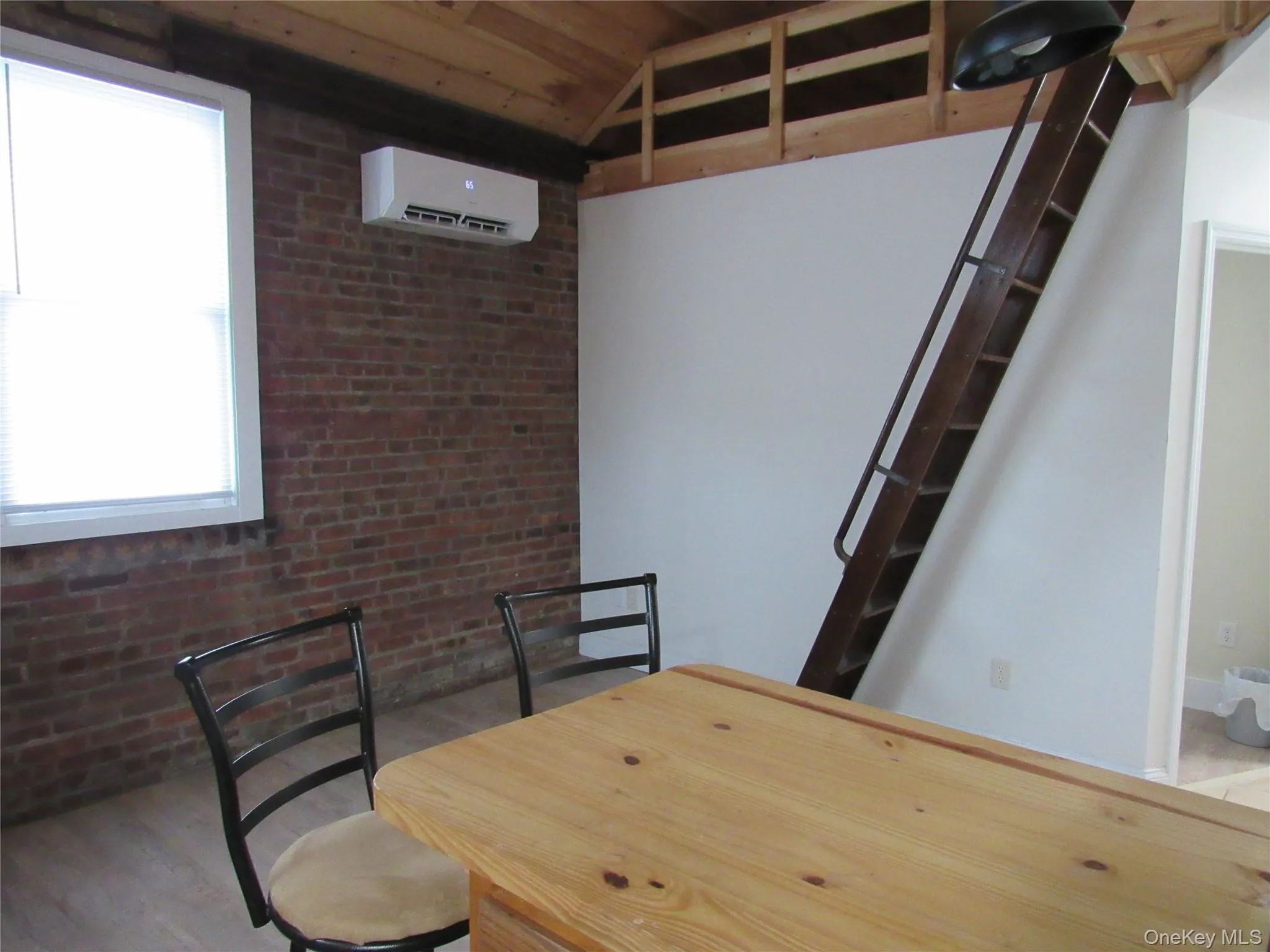 Dining area with a wall mounted AC, brick wall, and light wood-style floors Dining area with a wall mounted AC, brick wall, and light wood-style floors
