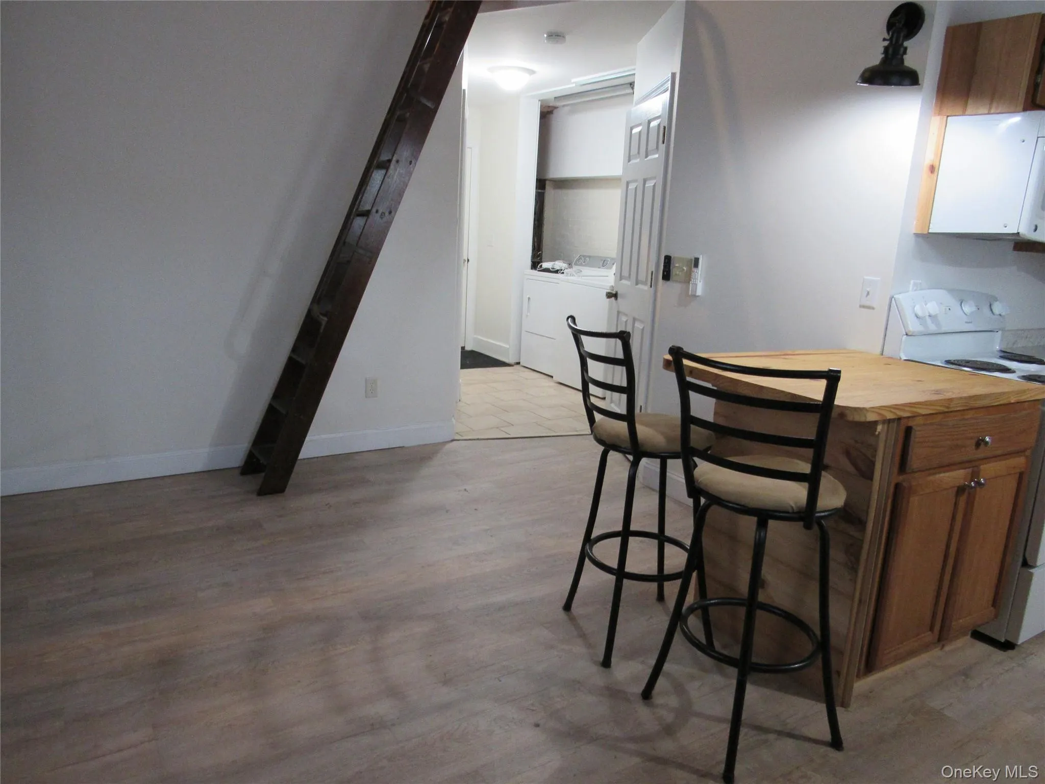 Kitchen with white electric range, a breakfast bar area, washer and dryer, light wood finished floors, and brown cabinetry Kitchen with white electric range, a breakfast bar area, washer and dryer, light wood finished floors, and brown cabinetry