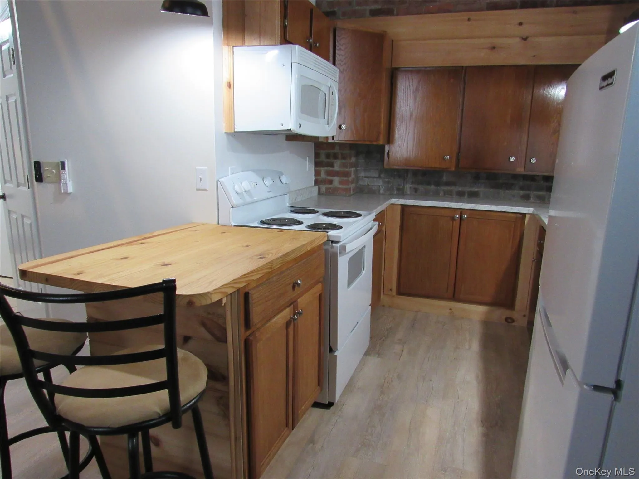 Kitchen with brown cabinetry, white appliances, wood counters, and backsplash Kitchen with brown cabinetry, white appliances, wood counters, and backsplash