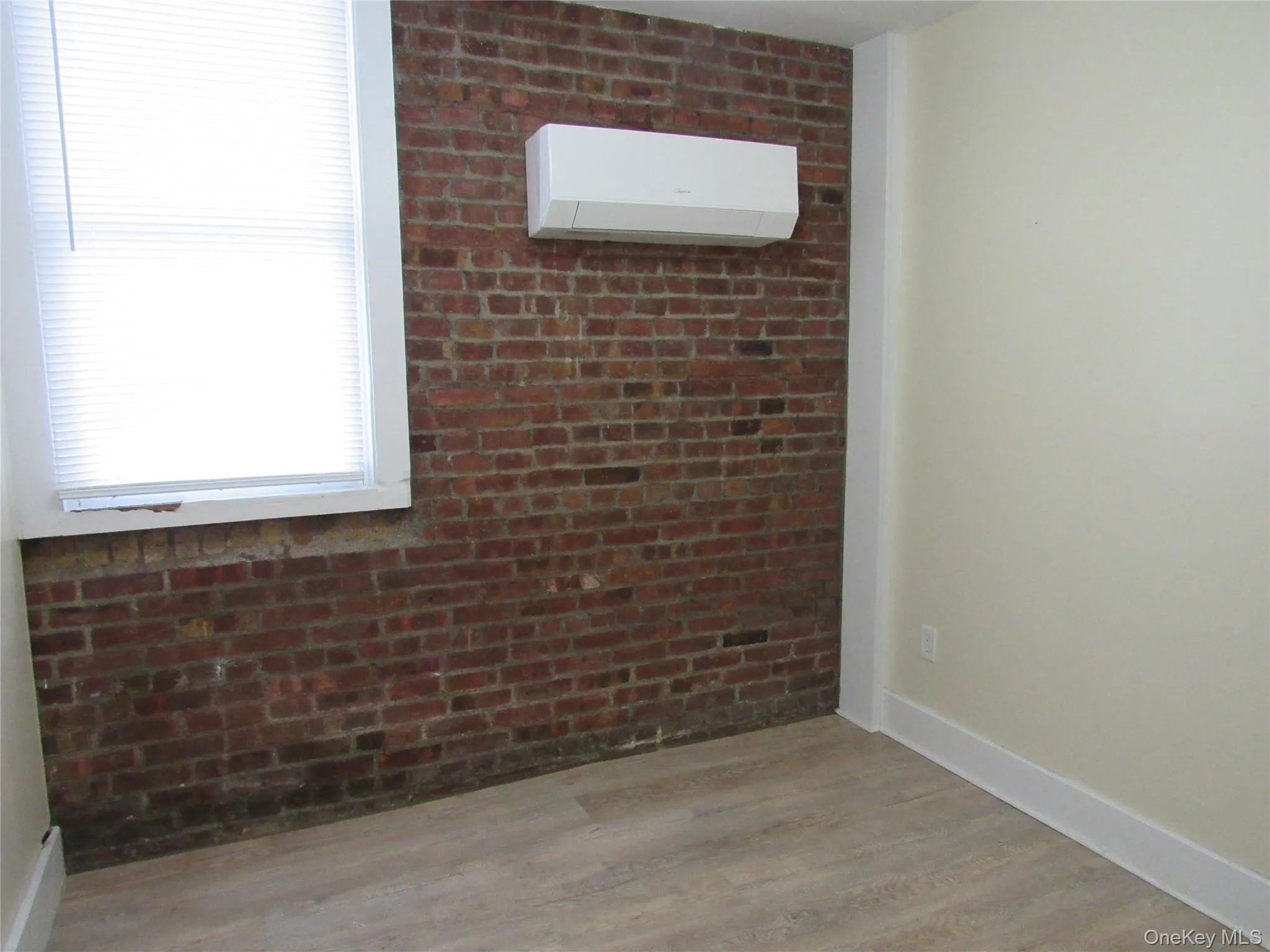 Unfurnished Bedroom featuring brick wall, light wood-style flooring, and a wall mounted AC Unfurnished Bedroom featuring brick wall, light wood-style flooring, and a wall mounted AC
