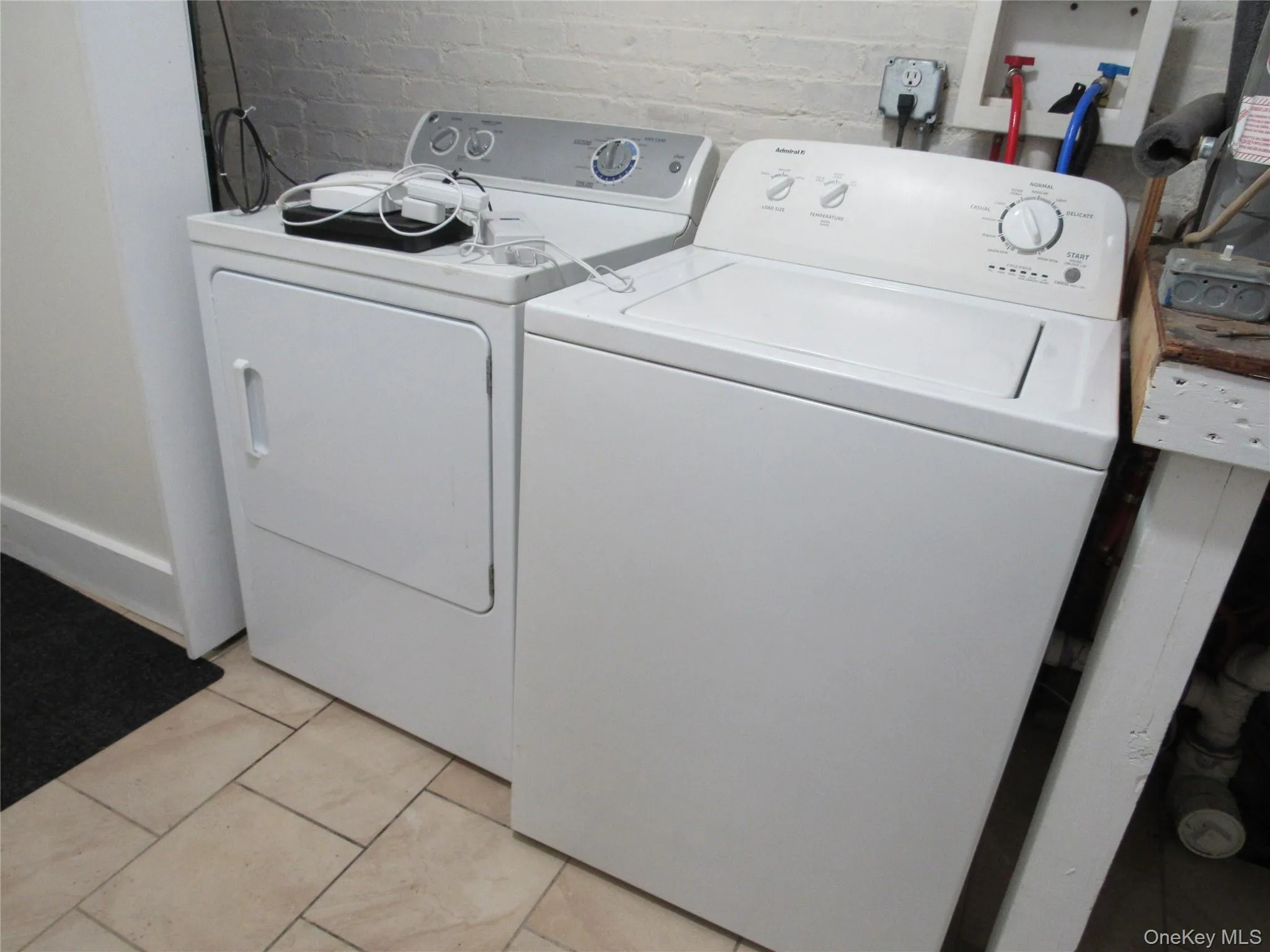 Laundry room with washing machine and dryer, brick wall, and light tile patterned floors Laundry room with washing machine and dryer, brick wall, and light tile patterned floors