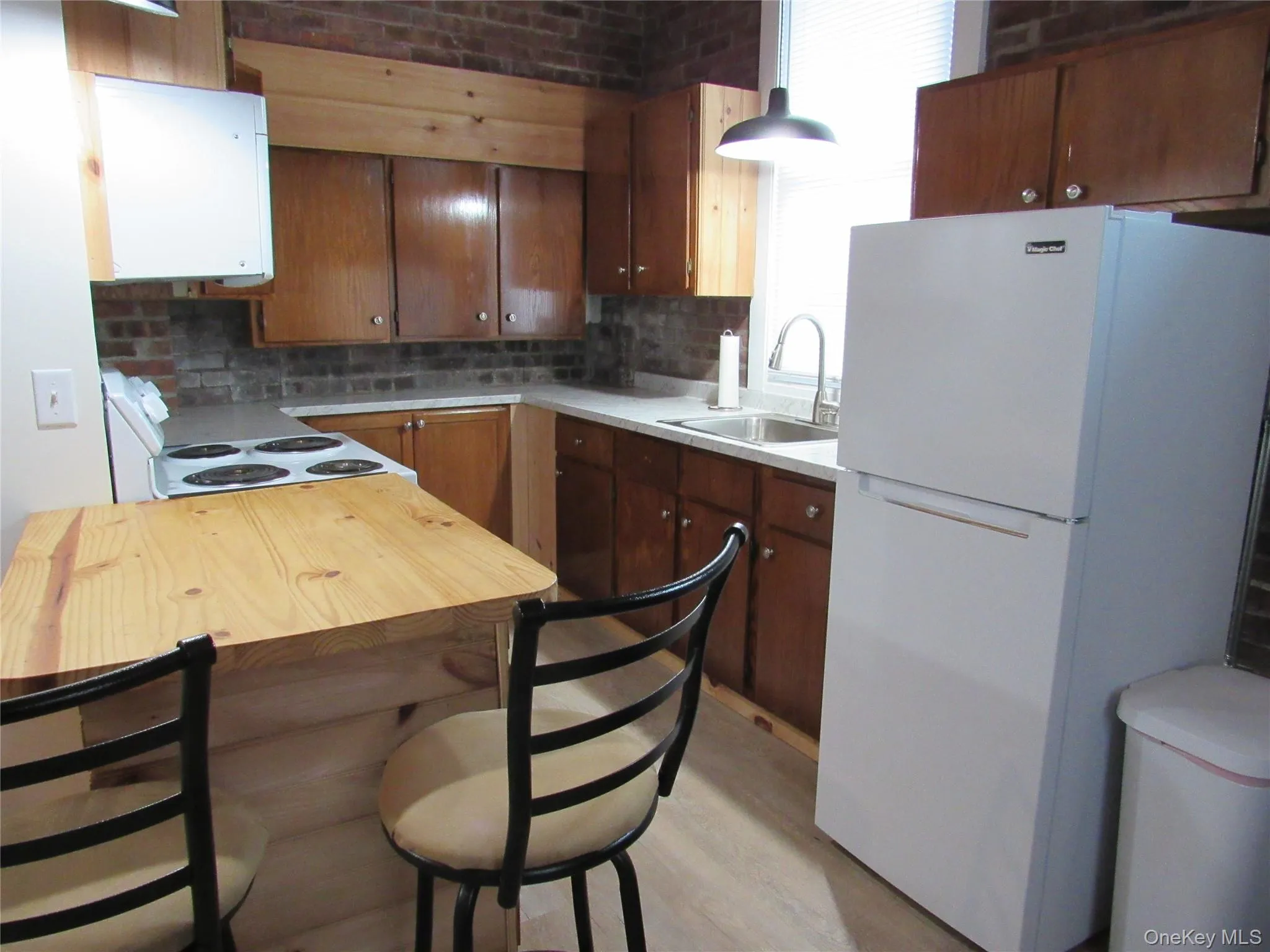 Kitchen featuring white appliances, backsplash, light wood-style floors, a kitchen breakfast bar, and brown cabinets Kitchen featuring white appliances, backsplash, light wood-style floors, a kitchen breakfast bar, and brown cabinets