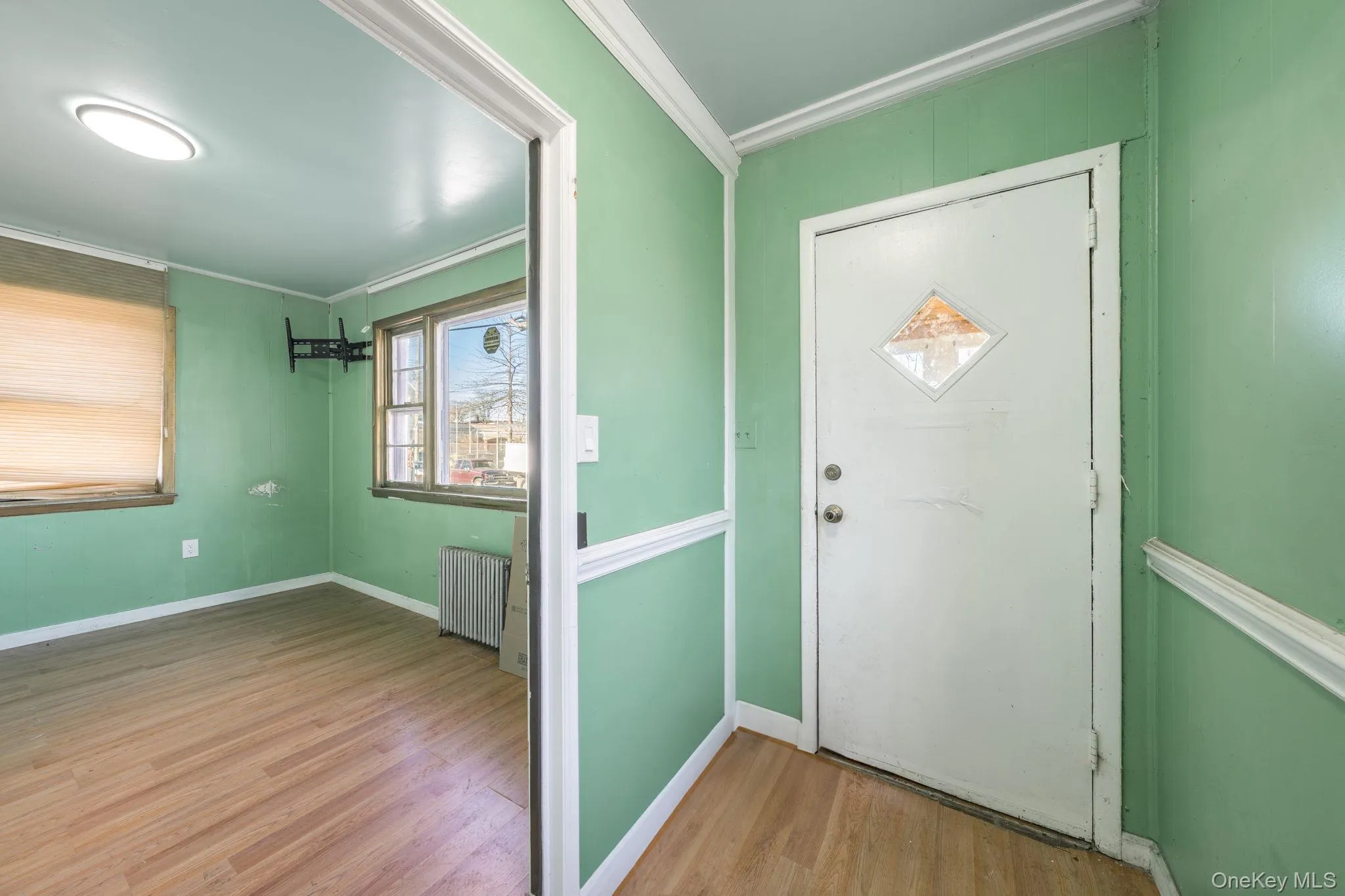 Foyer entrance featuring ornamental molding, radiator heating unit, and light wood finished floors Foyer entrance featuring ornamental molding, radiator heating unit, and light wood finished floors