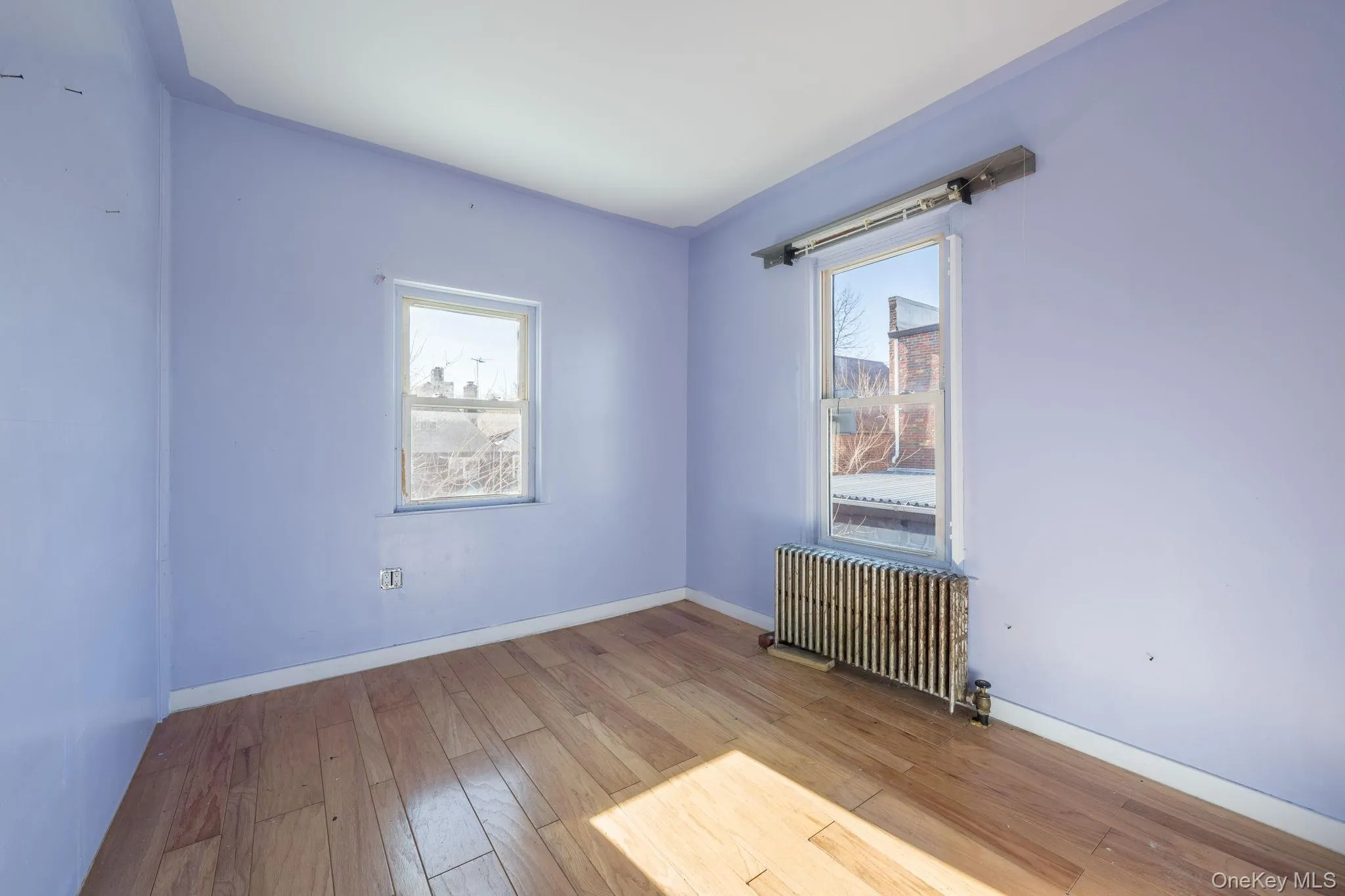 Empty room featuring radiator heating unit and hardwood / wood-style flooring Empty room featuring radiator heating unit and hardwood / wood-style flooring
