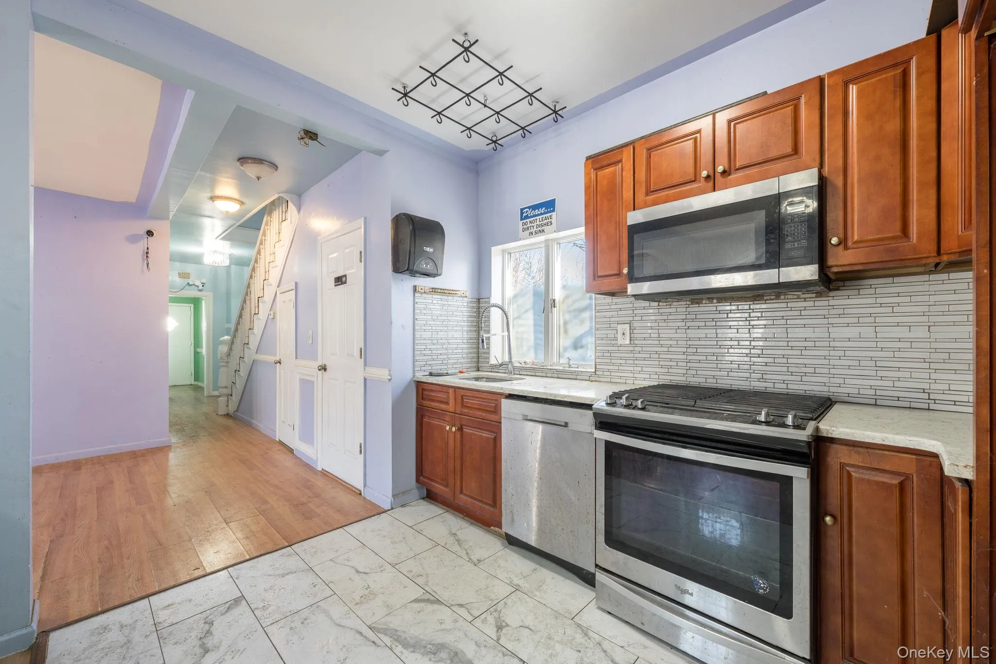 Kitchen featuring appliances with stainless steel finishes, light marble finish floors, backsplash, brown cabinetry, and light stone countertops Kitchen featuring appliances with stainless steel finishes, light marble finish floors, backsplash, brown cabinetry, and light stone countertops