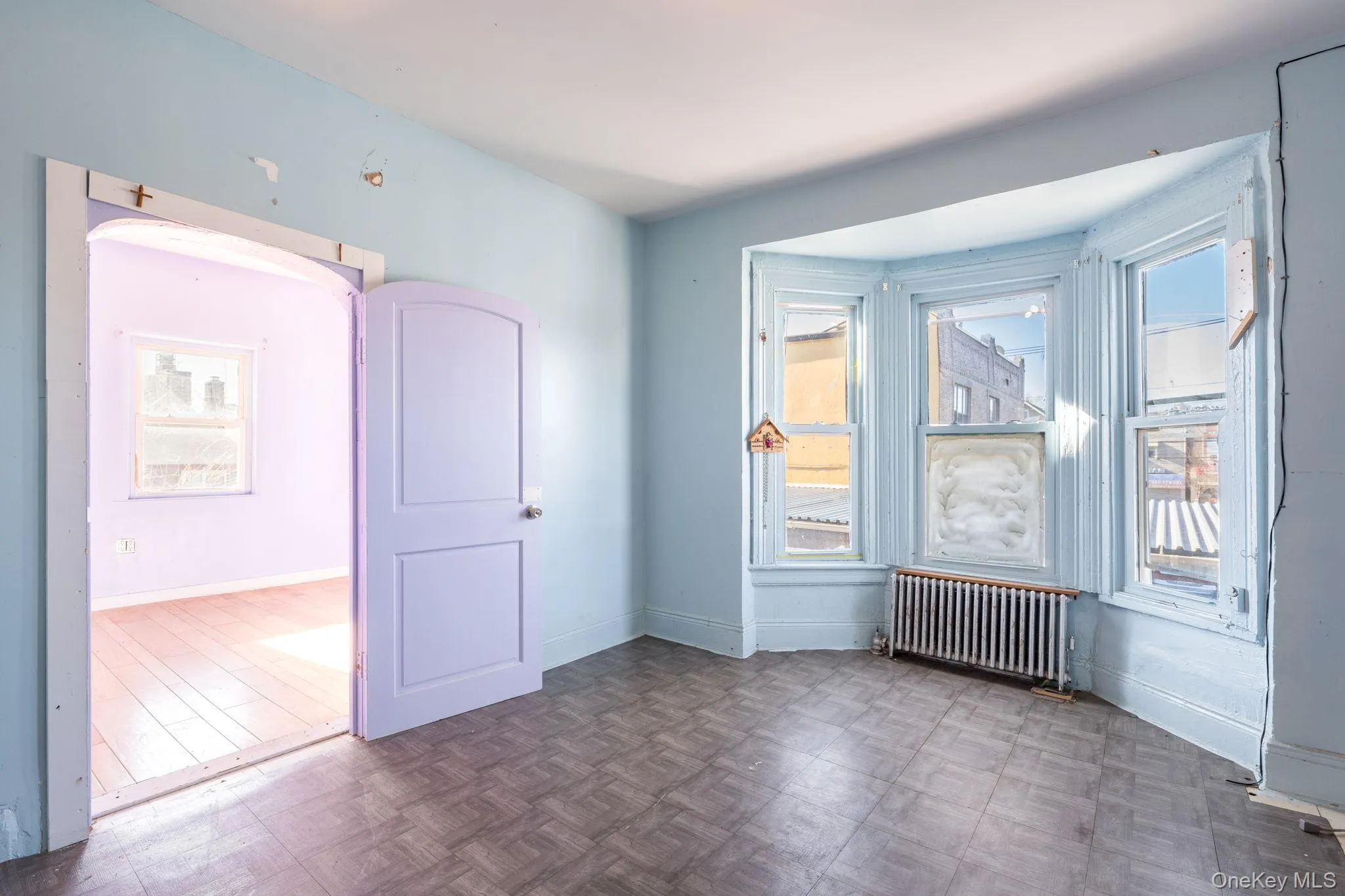 Empty room featuring radiator heating unit, healthy amount of natural light, parquet floors, and arched walkways Empty room featuring radiator heating unit, healthy amount of natural light, parquet floors, and arched walkways