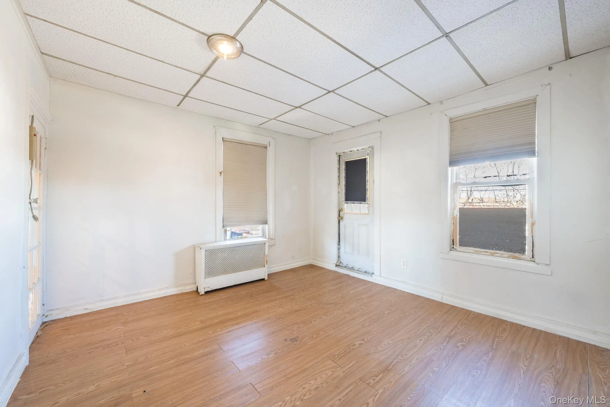 Unfurnished room with radiator heating unit, wood finished floors, and a drop ceiling Unfurnished room with radiator heating unit, wood finished floors, and a drop ceiling