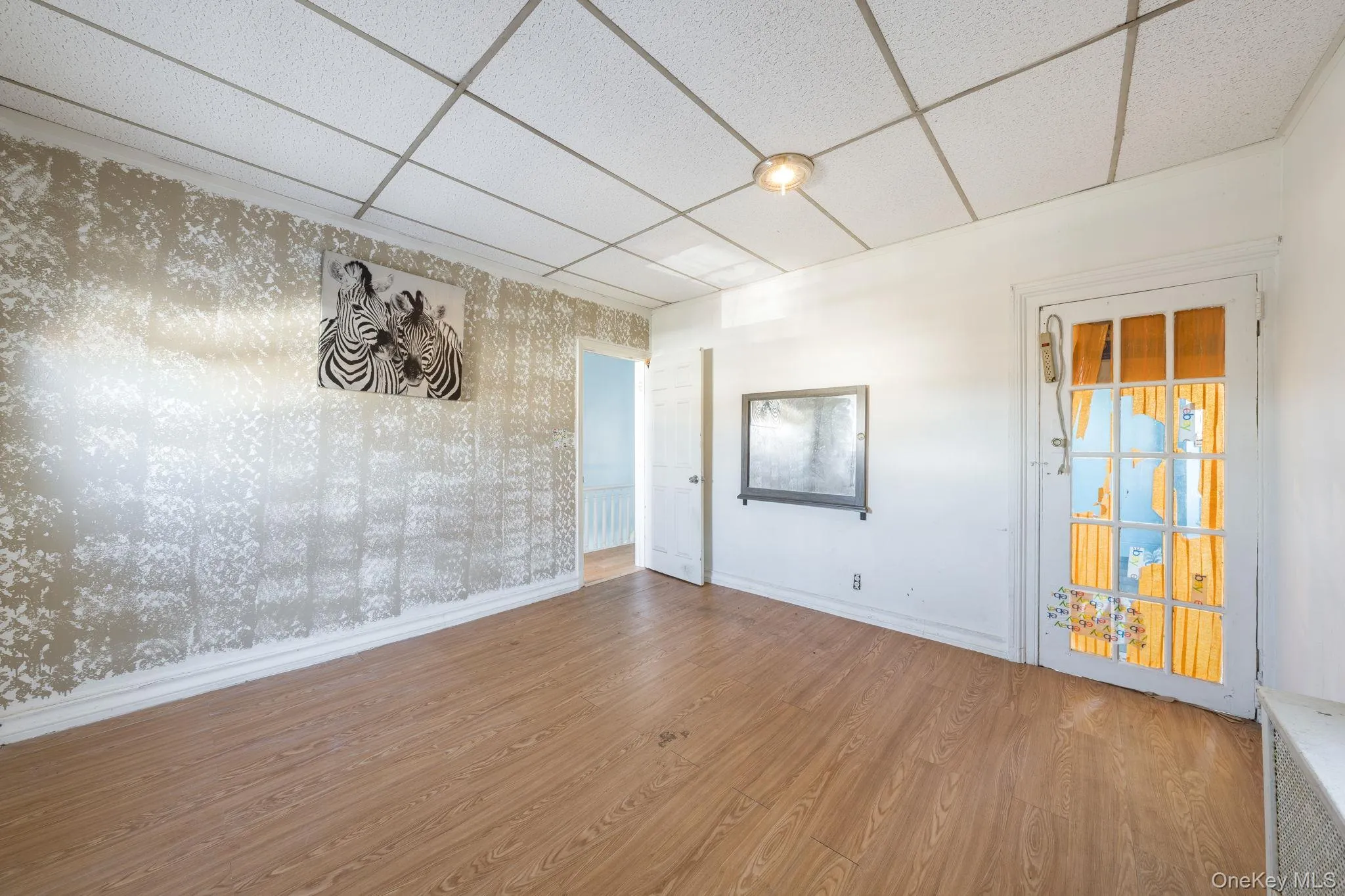 Empty room with a paneled ceiling, wood finished floors, and wallpapered walls Empty room with a paneled ceiling, wood finished floors, and wallpapered walls