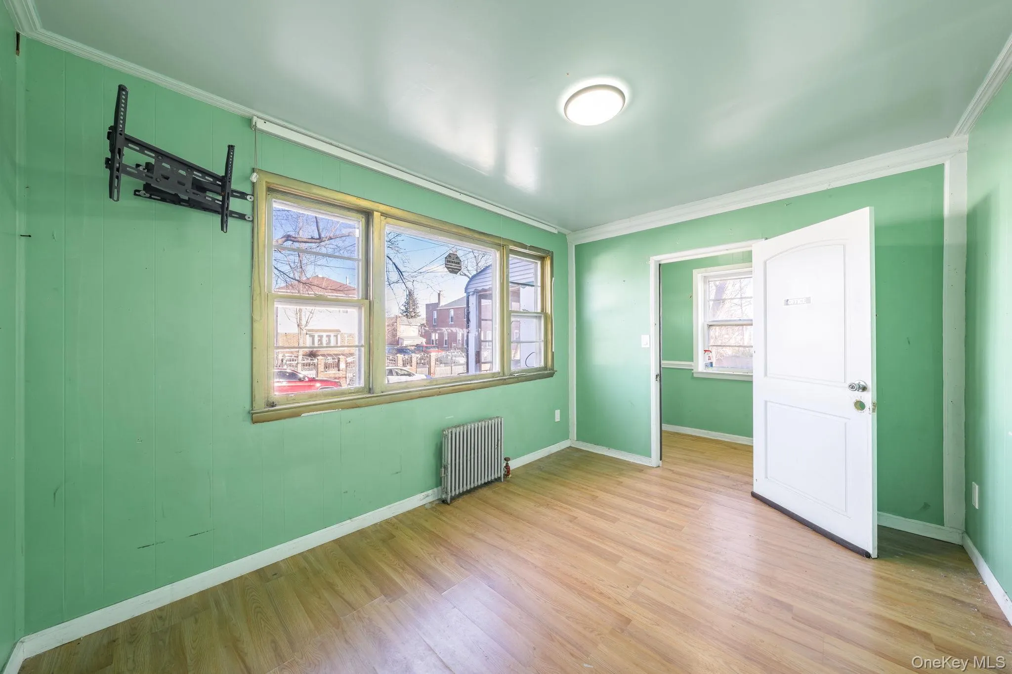 Unfurnished bedroom featuring radiator heating unit, crown molding, multiple windows, and wood finished floors Unfurnished bedroom featuring radiator heating unit, crown molding, multiple windows, and wood finished floors