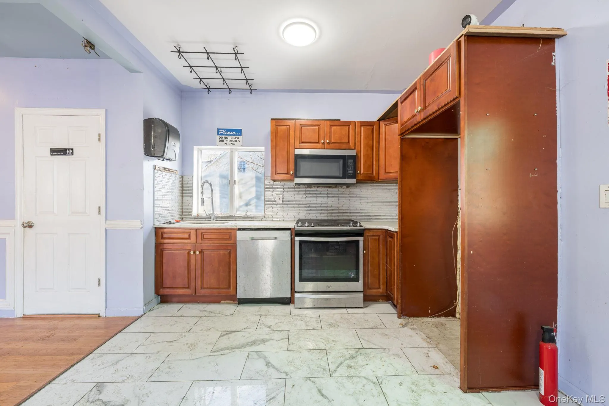 Kitchen with brown cabinets, appliances with stainless steel finishes, decorative backsplash, light countertops, and light marble finish flooring Kitchen with brown cabinets, appliances with stainless steel finishes, decorative backsplash, light countertops, and light marble finish flooring
