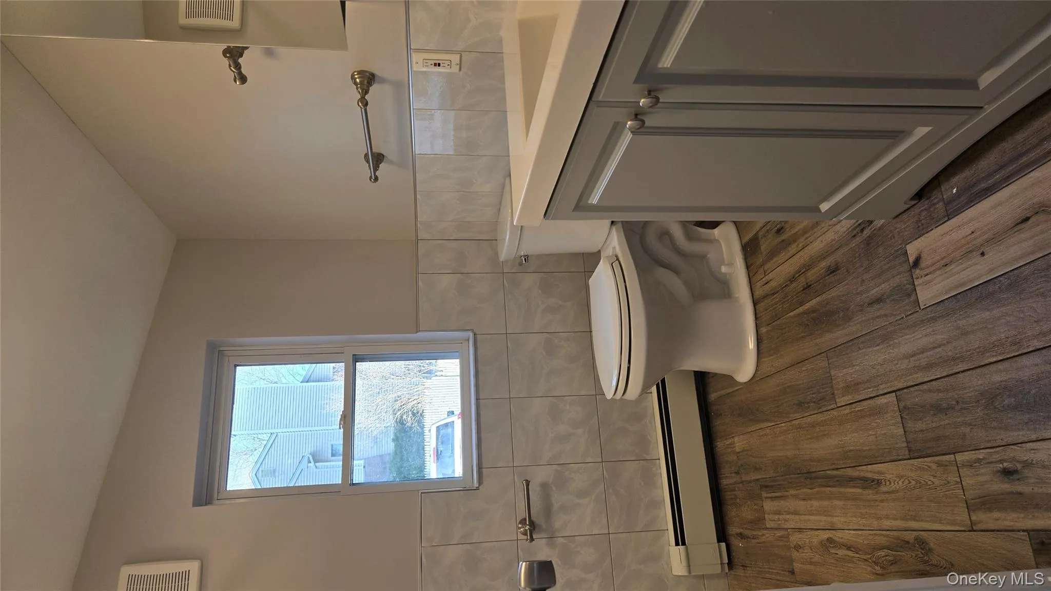 Half bath with vanity, wainscoting, a baseboard radiator, tile walls, and dark wood-style flooring Half bath with vanity, wainscoting, a baseboard radiator, tile walls, and dark wood-style flooring