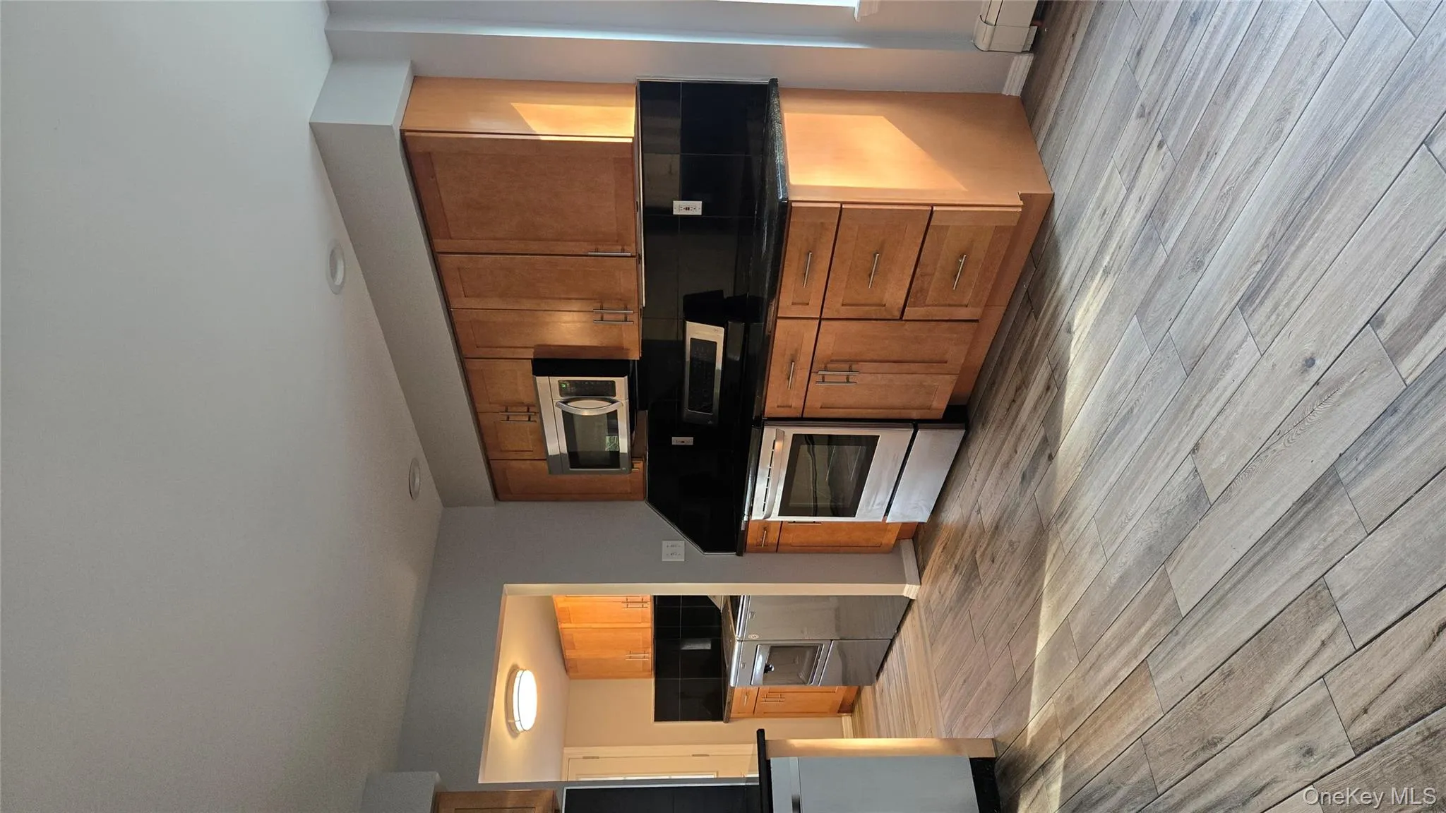 Kitchen featuring stainless steel electric stove, black microwave, brown cabinets, light wood finished floors, and backsplash Kitchen featuring stainless steel electric stove, black microwave, brown cabinets, light wood finished floors, and backsplash