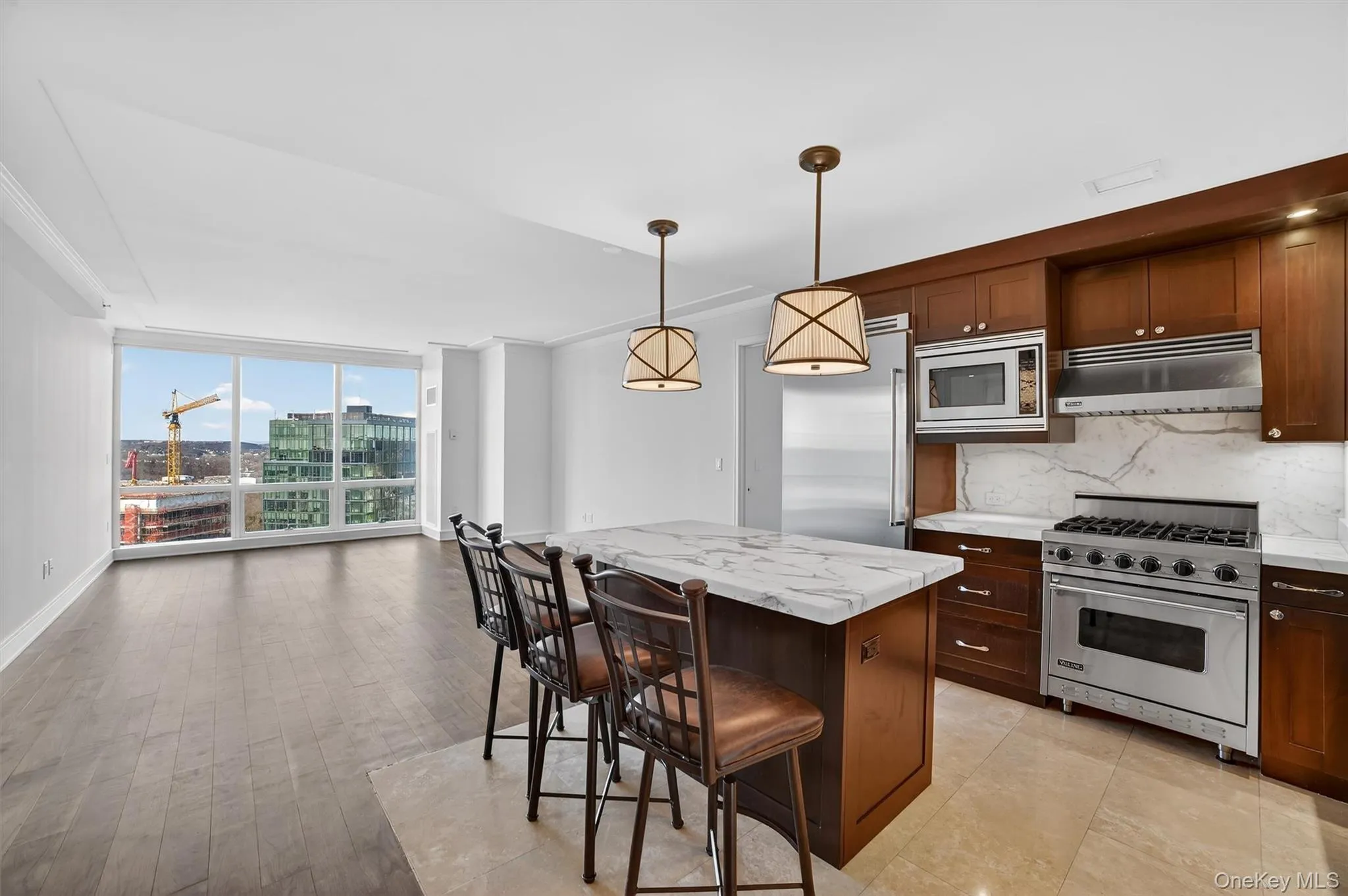 Kitchen with built in appliances, floor to ceiling windows, a kitchen breakfast bar, under cabinet range hood, and hanging light fixtures Kitchen with built in appliances, floor to ceiling windows, a kitchen breakfast bar, under cabinet range hood, and hanging light fixtures