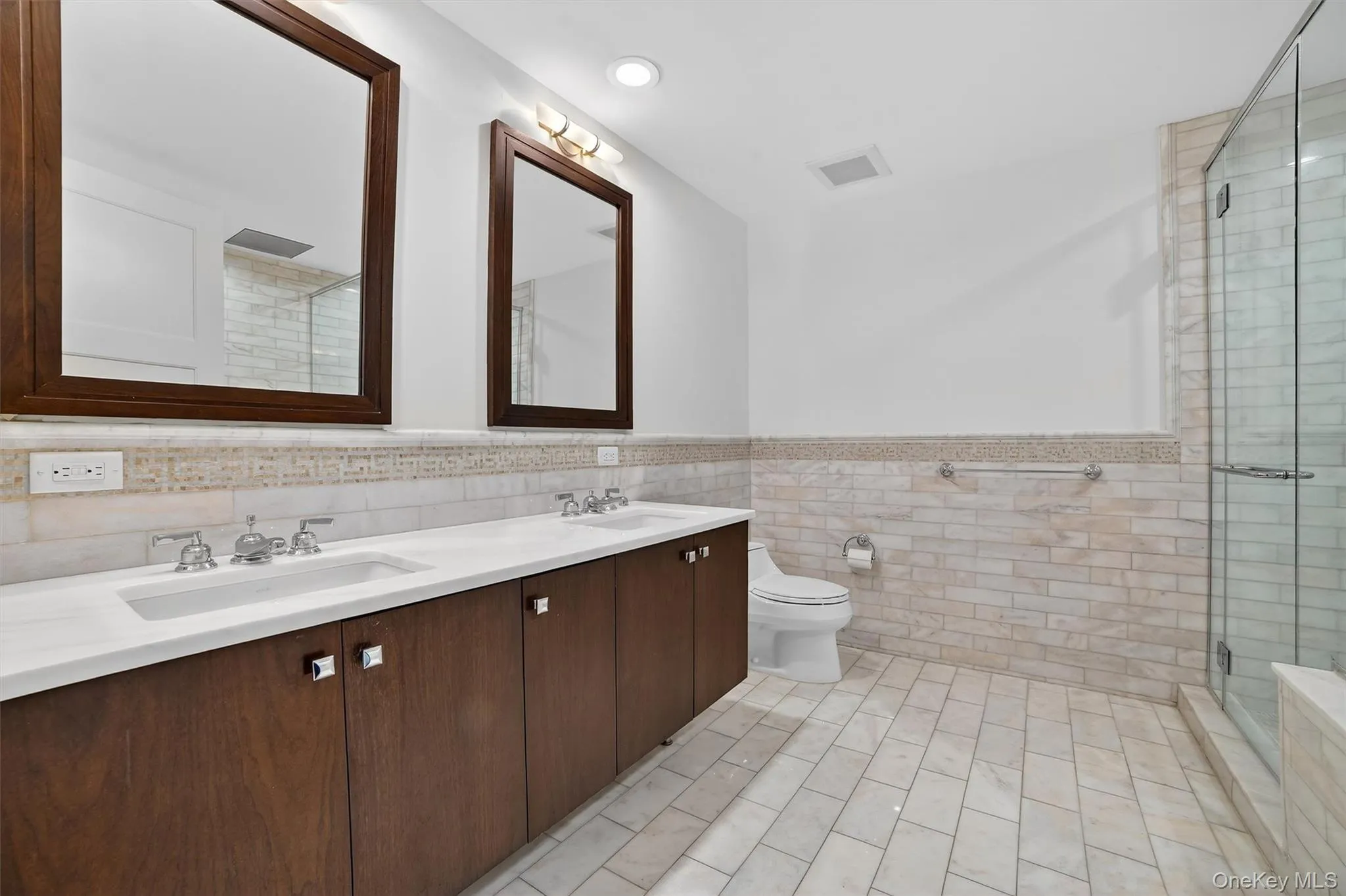 Bathroom with double vanity, wainscoting, a stall shower, and tile walls Bathroom with double vanity, wainscoting, a stall shower, and tile walls