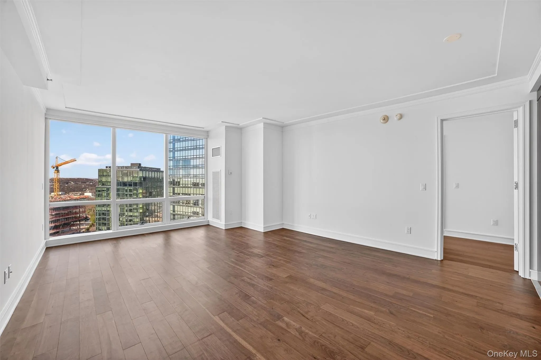 Empty room with a wall of windows, dark wood-type flooring, a view of city, and ornamental molding Empty room with a wall of windows, dark wood-type flooring, a view of city, and ornamental molding