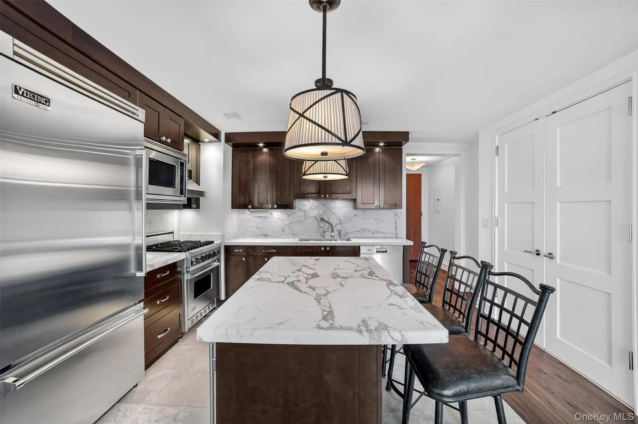 Kitchen with built in appliances, dark brown cabinetry, a kitchen island, hanging light fixtures, and backsplash Kitchen with built in appliances, dark brown cabinetry, a kitchen island, hanging light fixtures, and backsplash