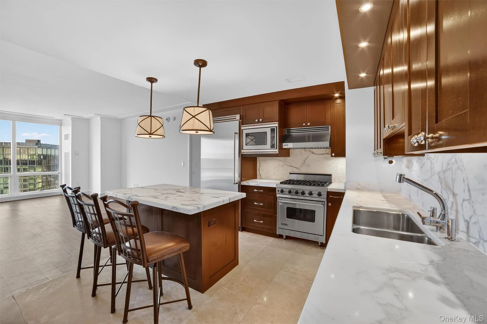 Kitchen featuring light stone counters, built in appliances, a kitchen island, a kitchen breakfast bar, and decorative backsplash Kitchen featuring light stone counters, built in appliances, a kitchen island, a kitchen breakfast bar, and decorative backsplash