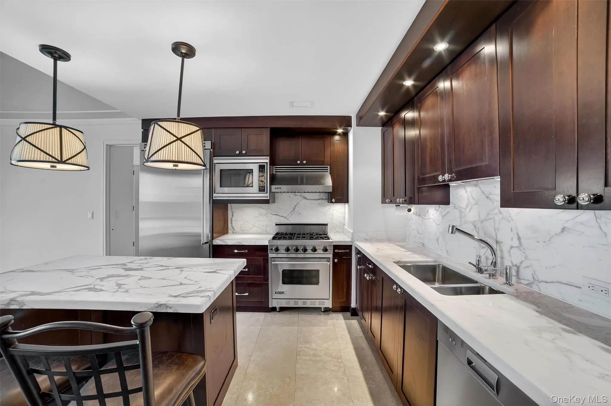 Kitchen with built in appliances, a breakfast bar area, light stone countertops, and under cabinet range hood Kitchen with built in appliances, a breakfast bar area, light stone countertops, and under cabinet range hood