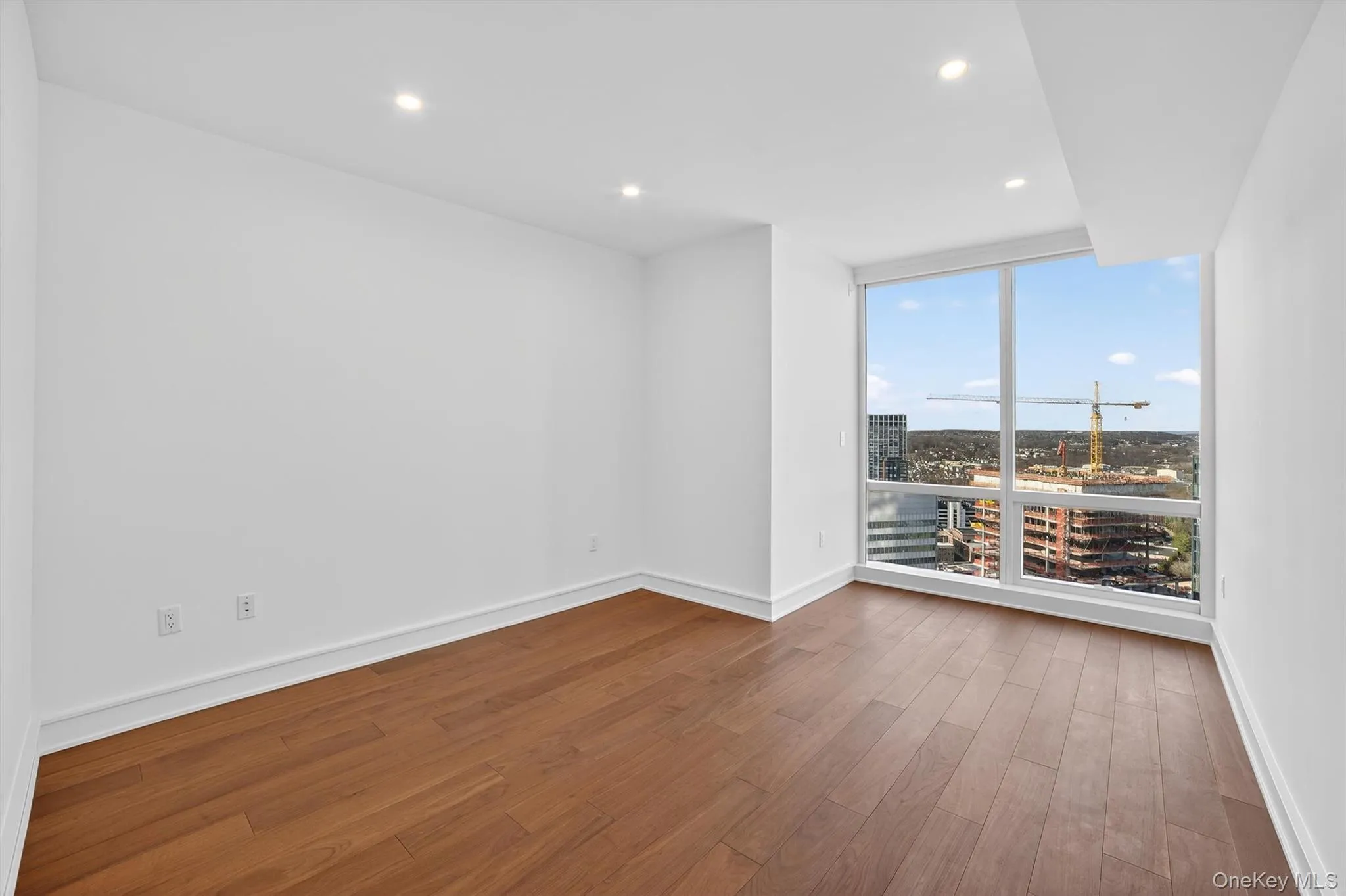 Spare room with recessed lighting, wood finished floors, floor to ceiling windows, and a view of city Spare room with recessed lighting, wood finished floors, floor to ceiling windows, and a view of city