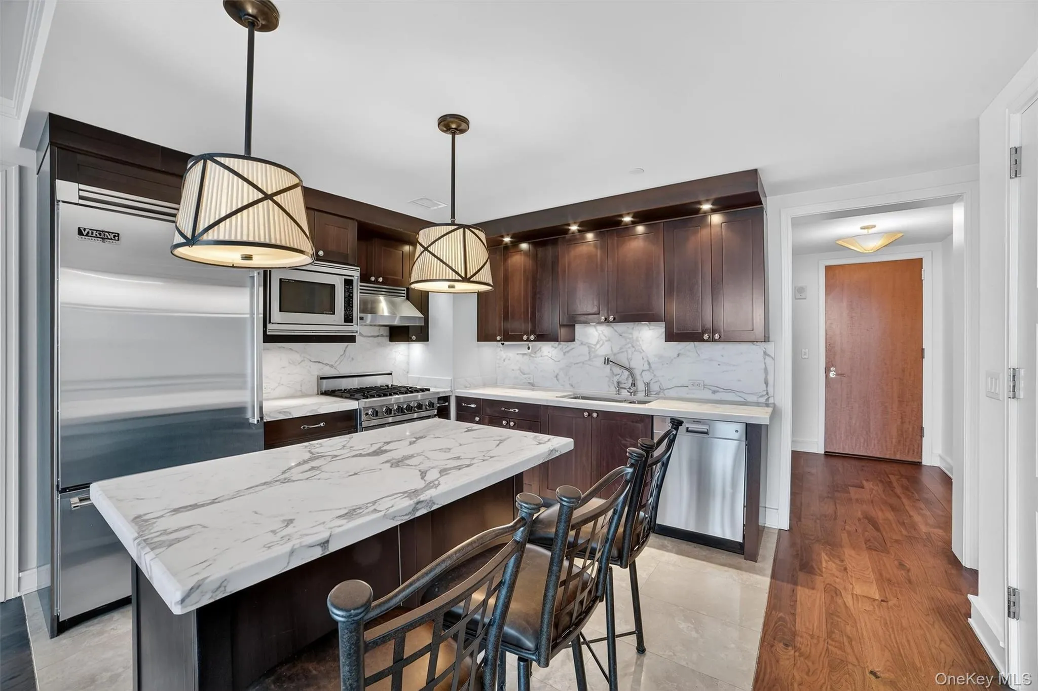 Kitchen featuring dark brown cabinets, built in appliances, decorative light fixtures, decorative backsplash, and a breakfast bar Kitchen featuring dark brown cabinets, built in appliances, decorative light fixtures, decorative backsplash, and a breakfast bar
