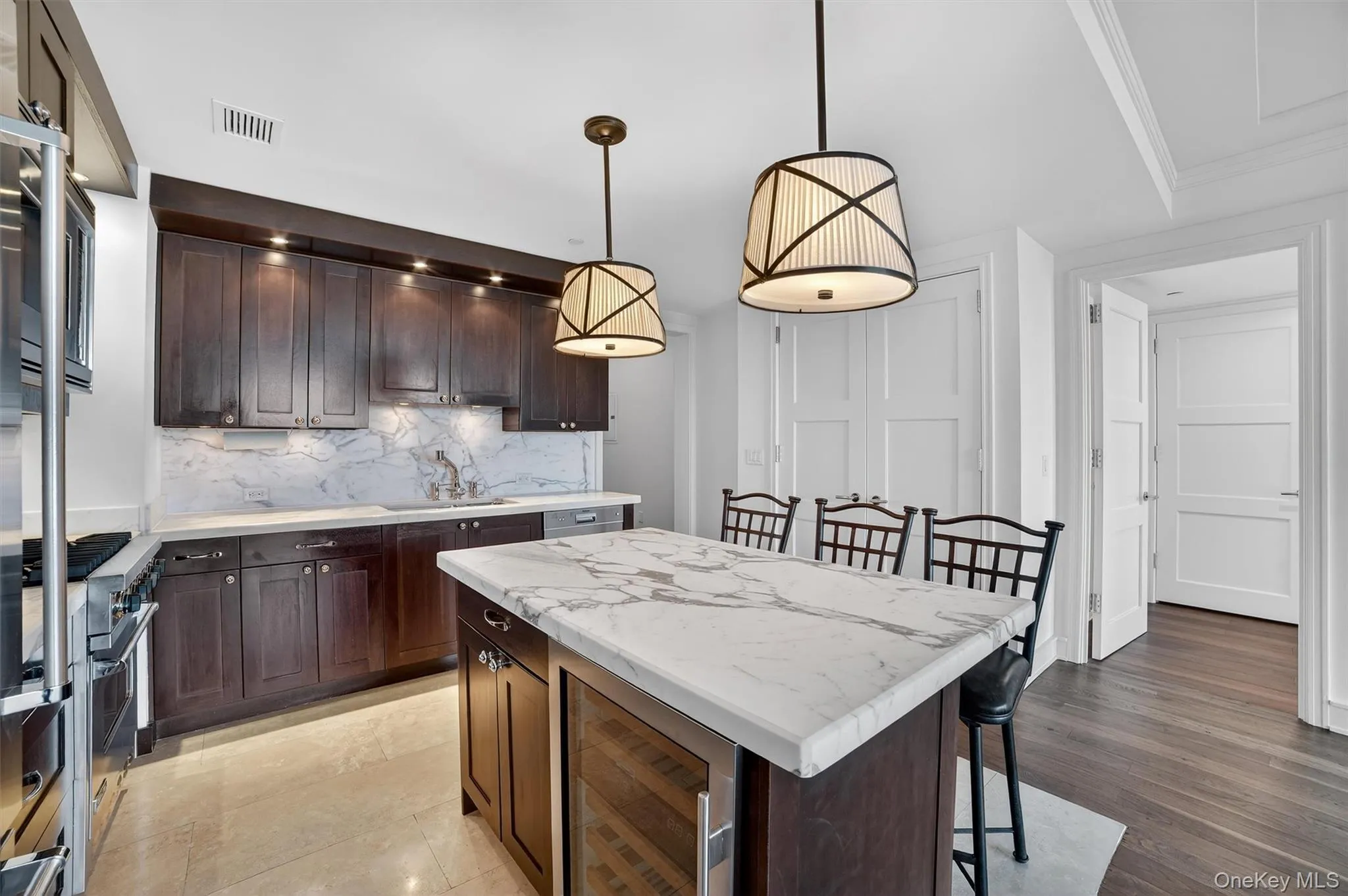 Kitchen featuring dark brown cabinetry, wine cooler, a kitchen breakfast bar, a center island, and light stone counters Kitchen featuring dark brown cabinetry, wine cooler, a kitchen breakfast bar, a center island, and light stone counters