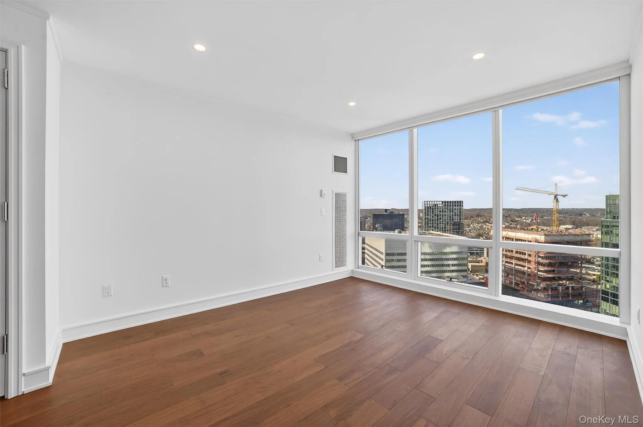Empty room with a wall of windows, dark wood-style flooring, recessed lighting, and a view of city Empty room with a wall of windows, dark wood-style flooring, recessed lighting, and a view of city