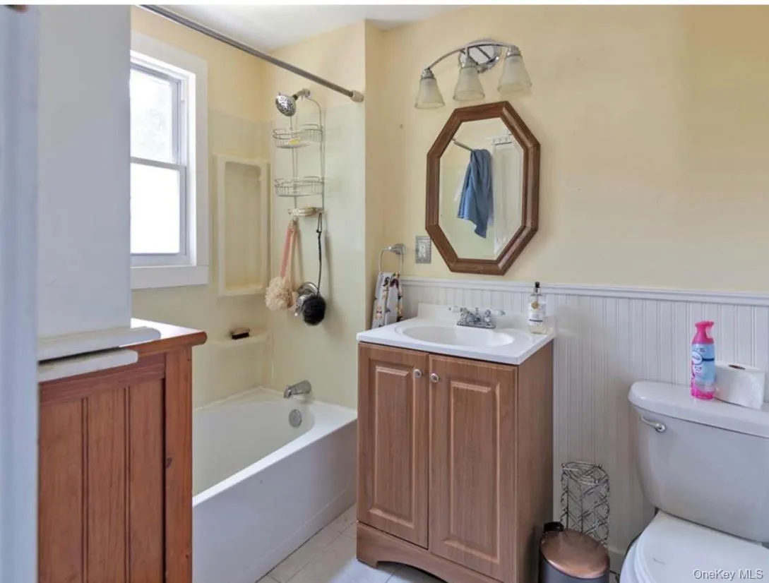Full bath featuring vanity, a wainscoted wall, shower / washtub combination, and light tile patterned floors Full bath featuring vanity, a wainscoted wall, shower / washtub combination, and light tile patterned floors