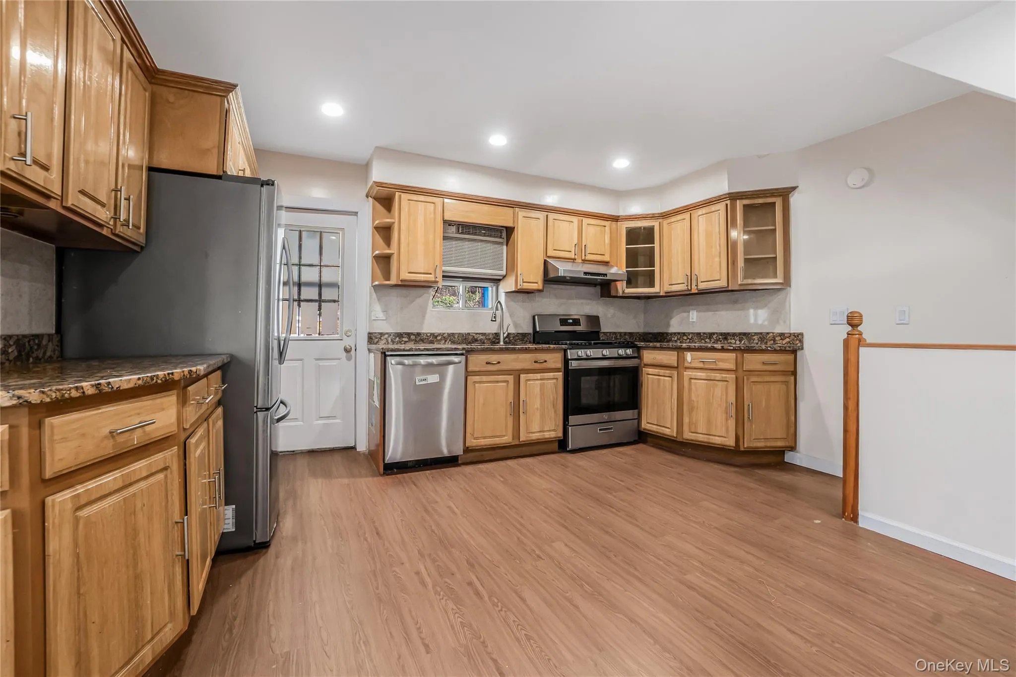 Kitchen with appliances with stainless steel finishes, light wood-type flooring, open shelves, glass insert cabinets, and tasteful backsplash Kitchen with appliances with stainless steel finishes, light wood-type flooring, open shelves, glass insert cabinets, and tasteful backsplash