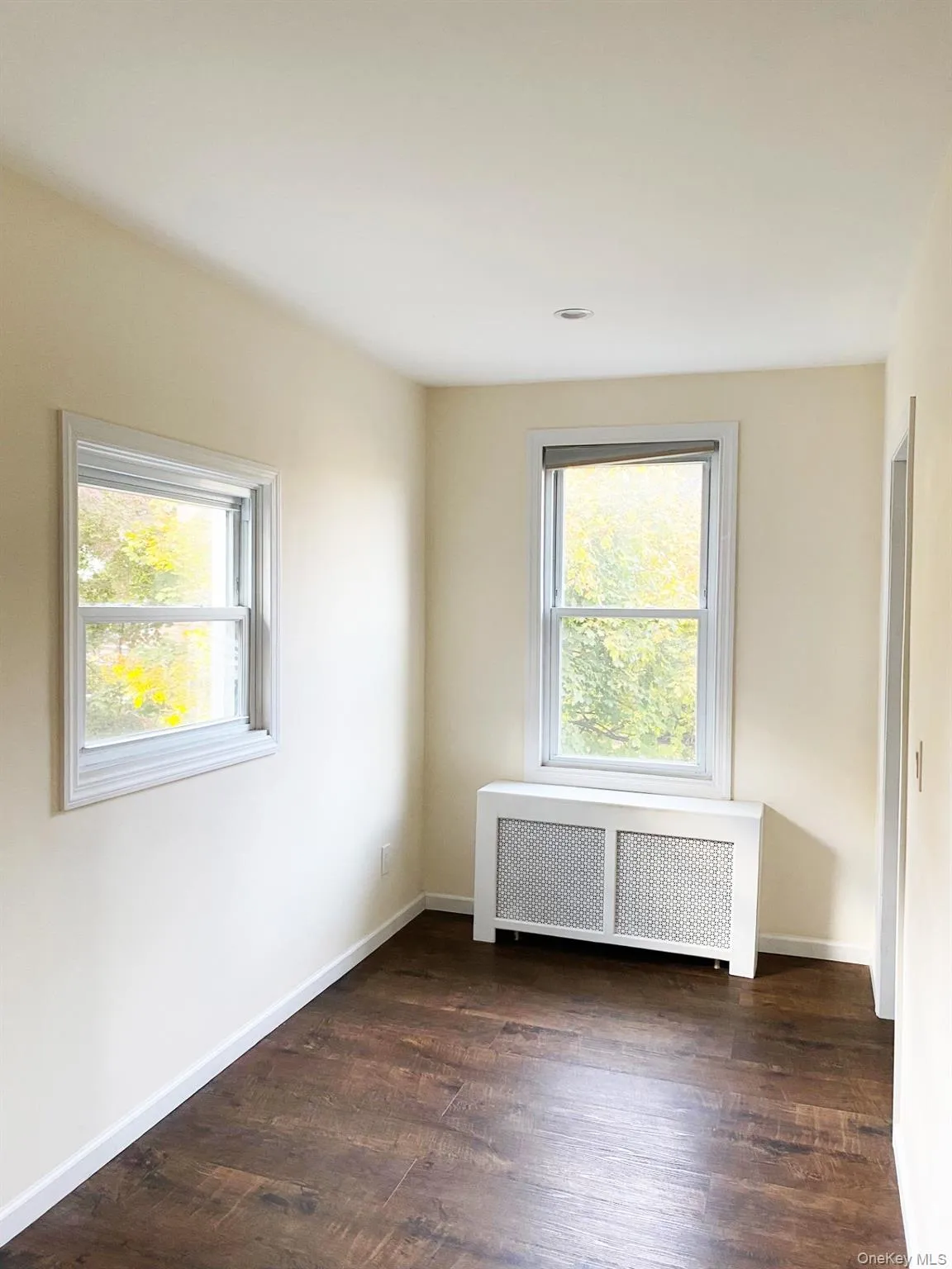 Empty room with radiator heating unit, dark wood-type flooring, and healthy amount of natural light Empty room with radiator heating unit, dark wood-type flooring, and healthy amount of natural light