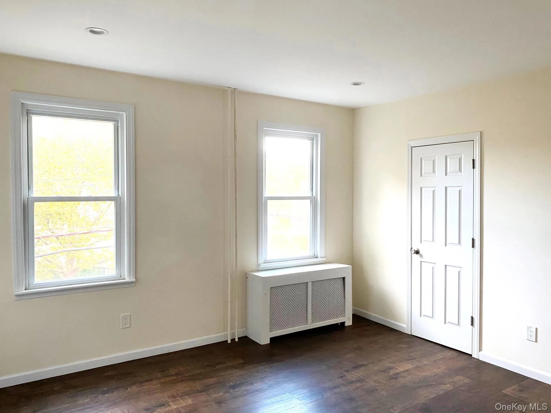 Empty room featuring radiator heating unit and dark wood-style flooring Empty room featuring radiator heating unit and dark wood-style flooring