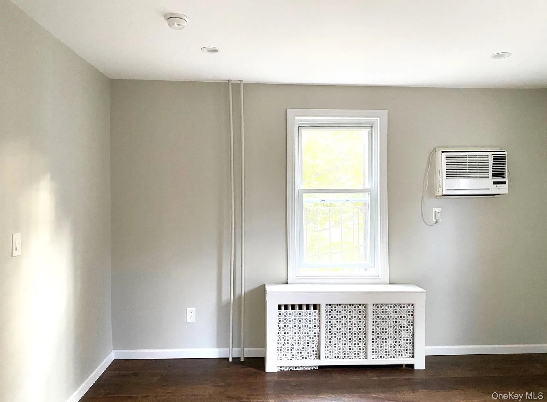 Unfurnished room with radiator heating unit, dark wood-style floors, and a wall mounted AC Unfurnished room with radiator heating unit, dark wood-style floors, and a wall mounted AC
